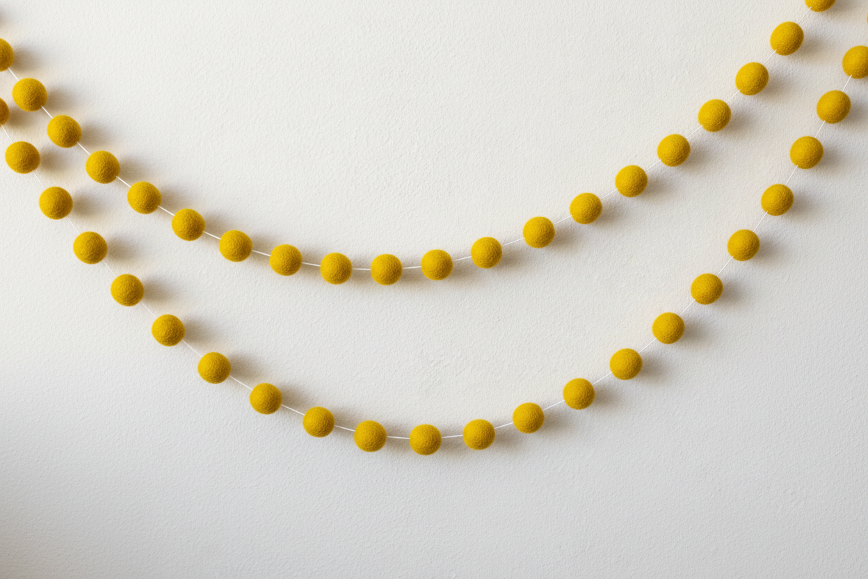 Guirlande de pompons unie jaune moutarde suspendue sur un mur blanc