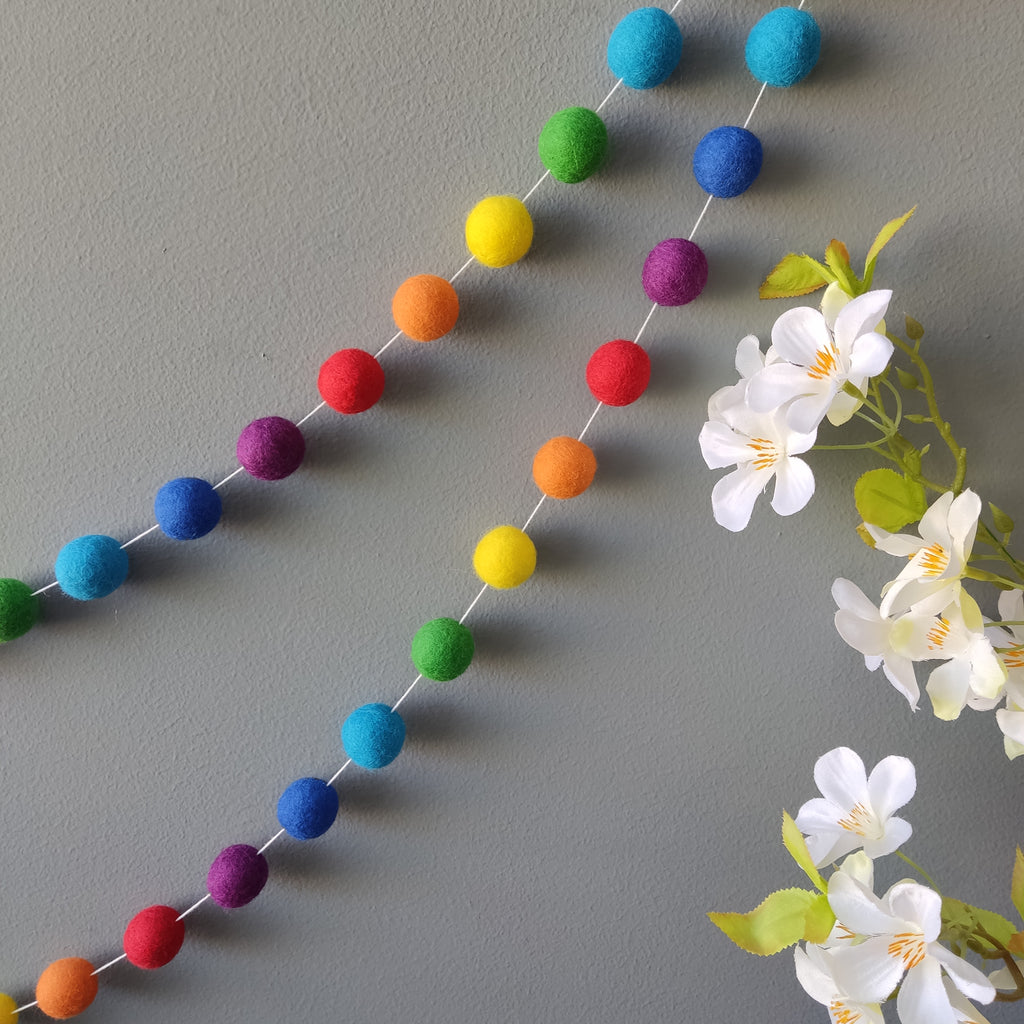 Guirlande de pompons aux couleurs arc-en-ciel vives accrochée sur un mur
