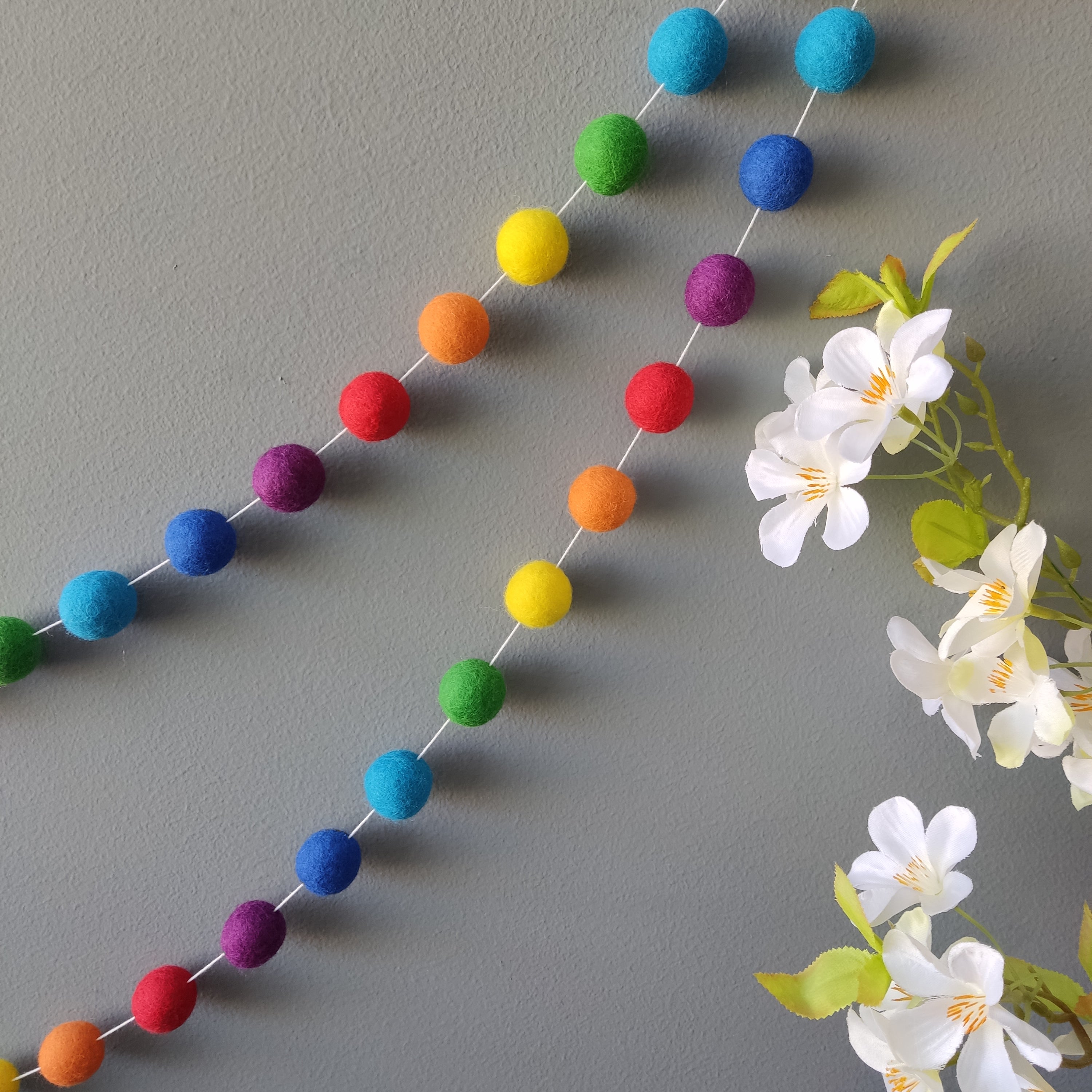 Guirlande de pompons aux couleurs arc-en-ciel vives accrochée sur un mur