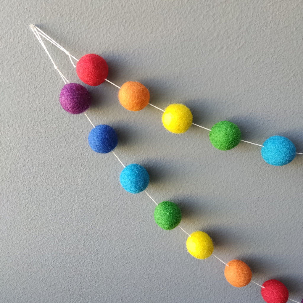 Guirlande de pompons de feutre arc-en-ciel vue de près montrant les boucles pour l'accrocher