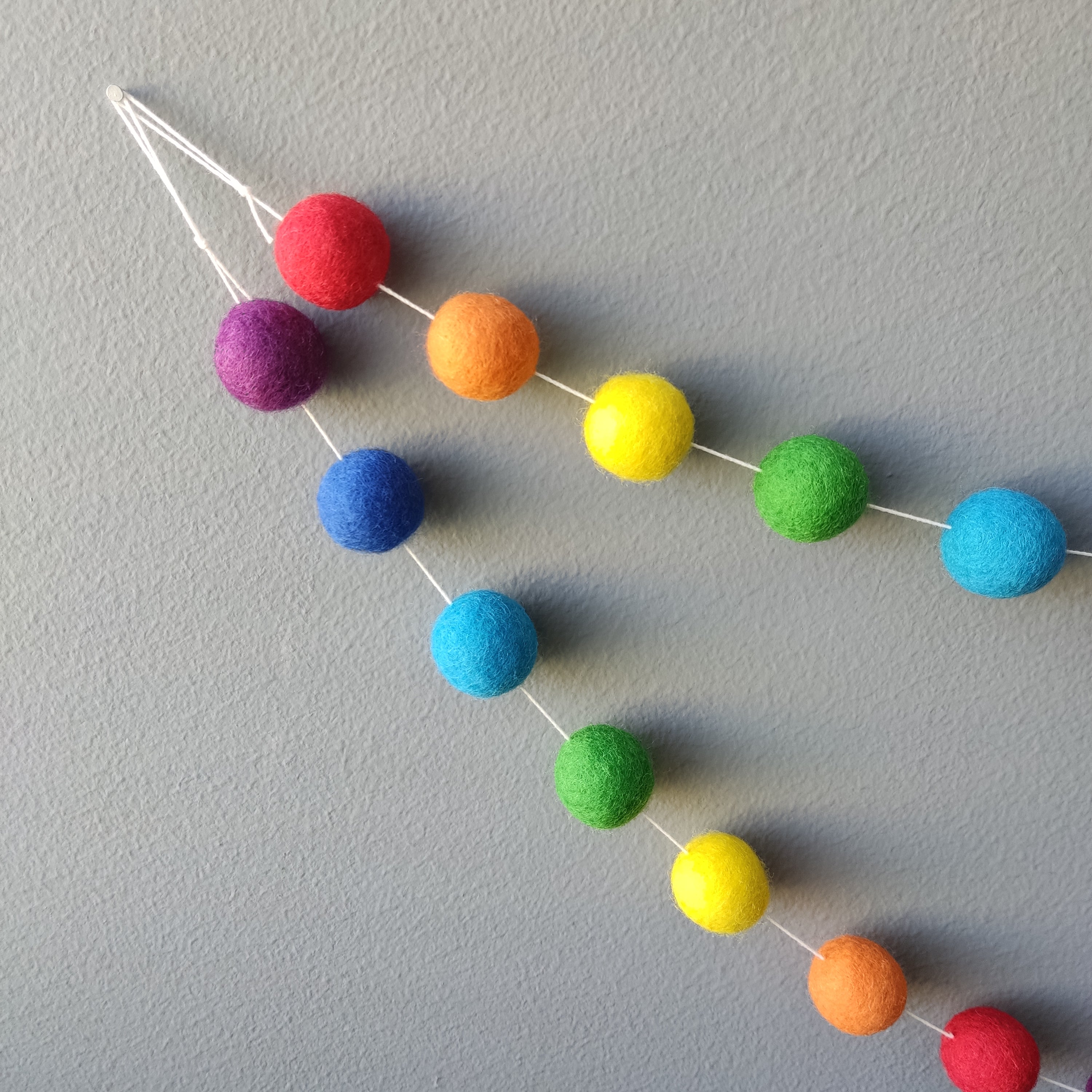 Guirlande de pompons de feutre arc-en-ciel vue de près montrant les boucles pour l'accrocher