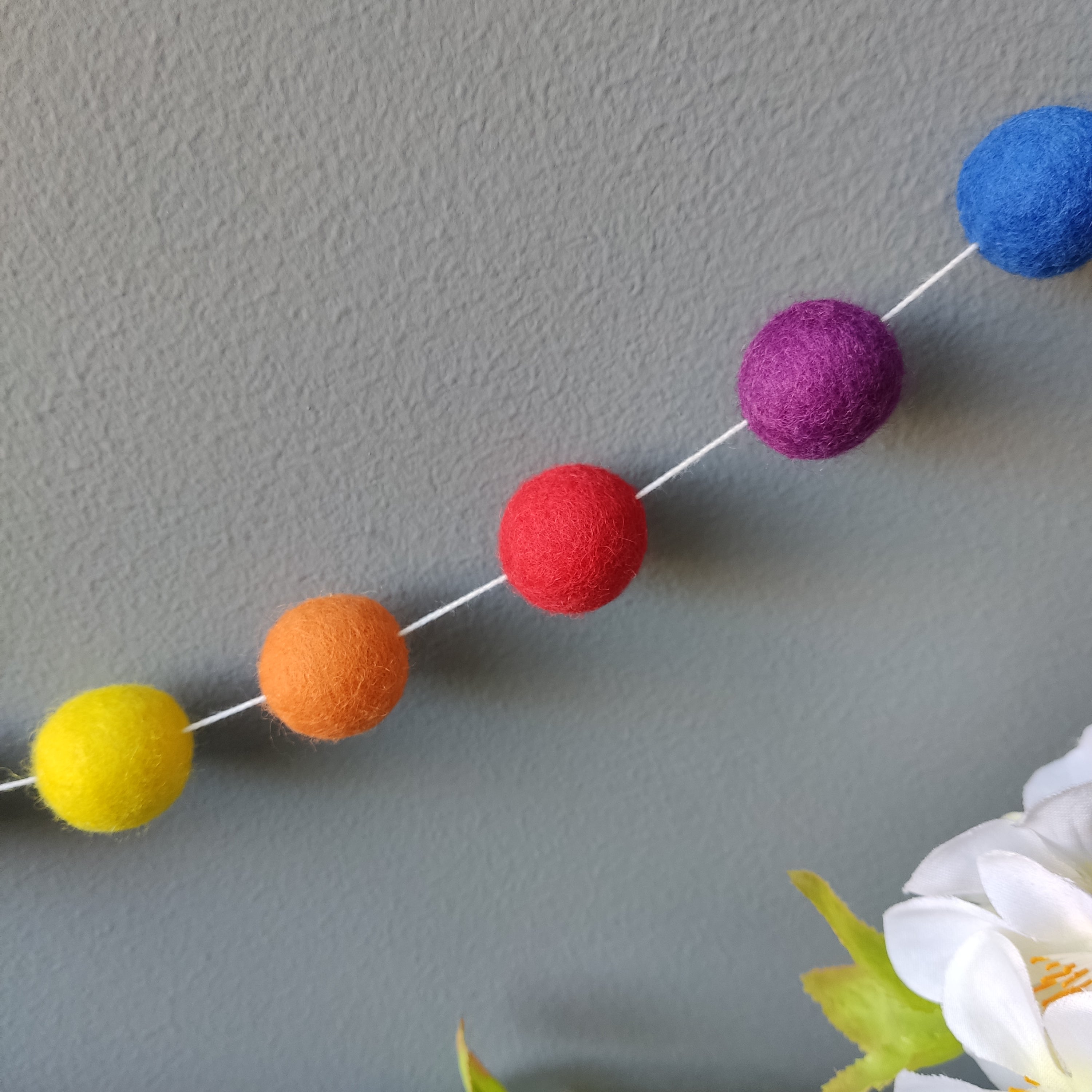 Zoom sur les boules de feutre de la guirlande de pompons aux couleurs arc-en-ciel vives