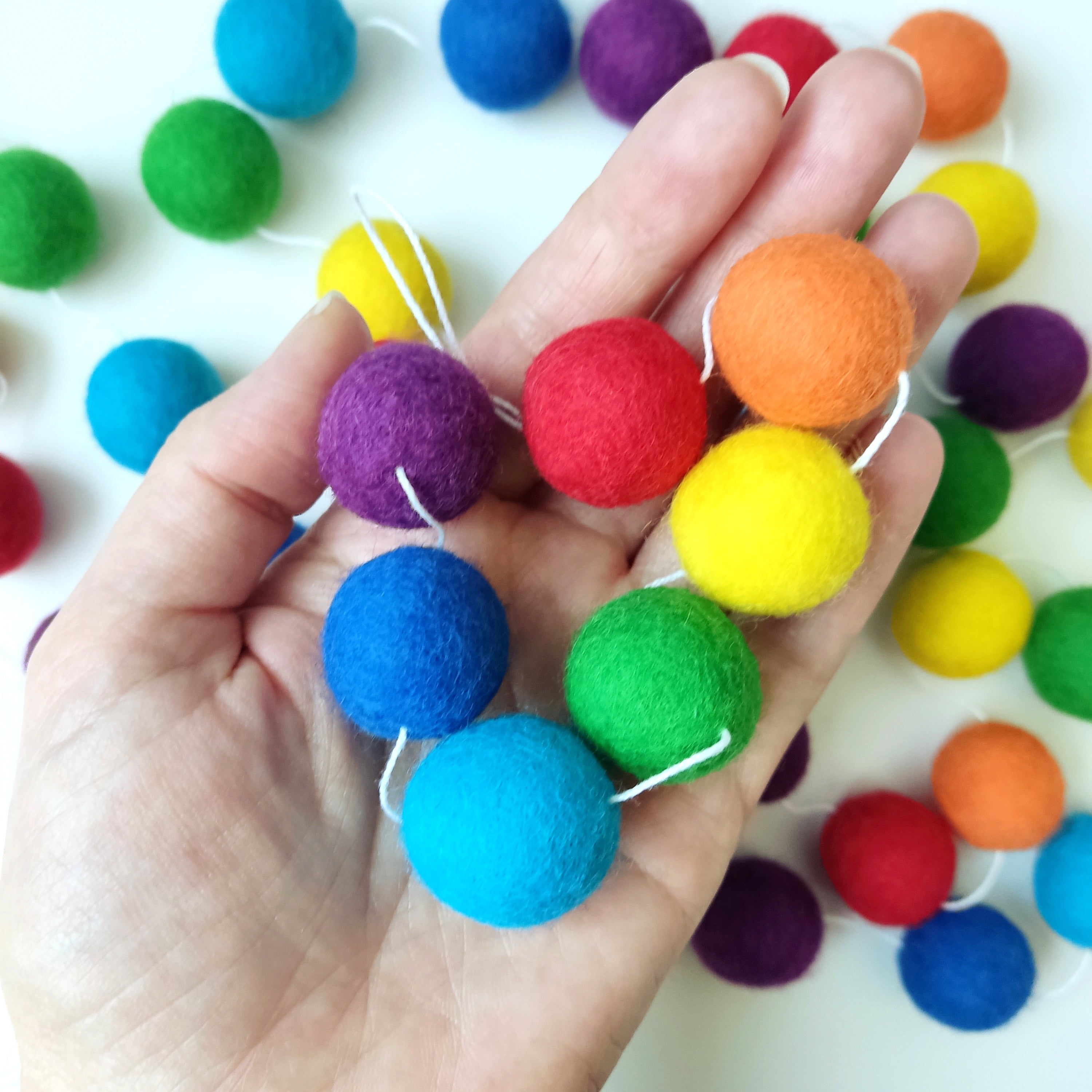 Pompons de la guirlande ar-en-ciel dans une main pour visualiser la taille des pompons