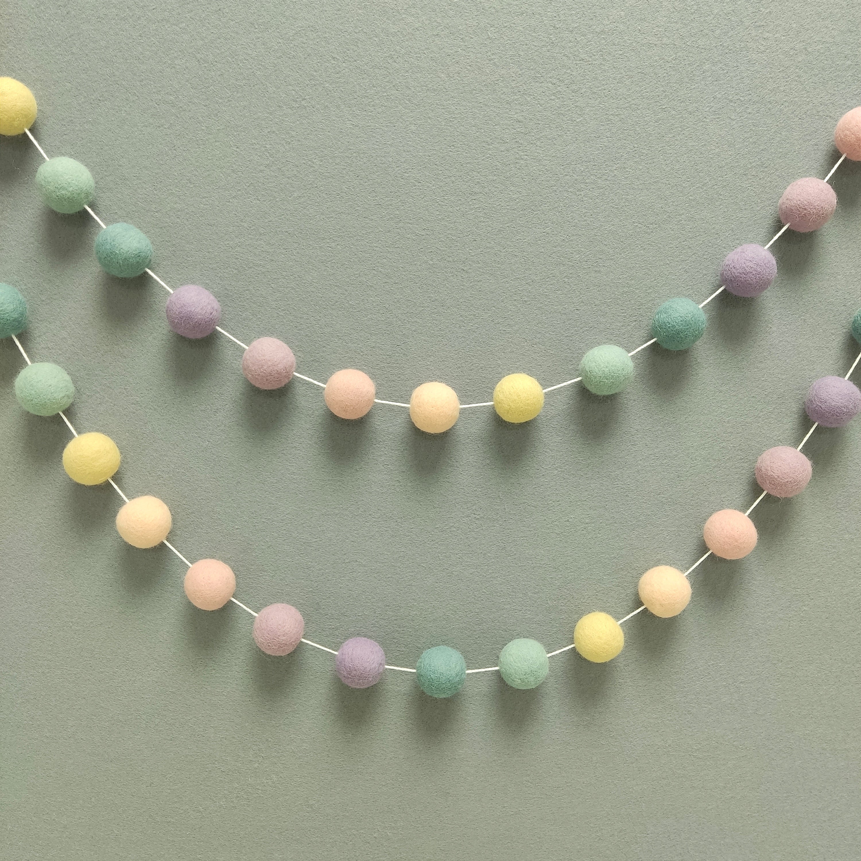 Guirlande de pompons feutrés aux couleurs arc-en-ciel pastel estompées pour décoration murale