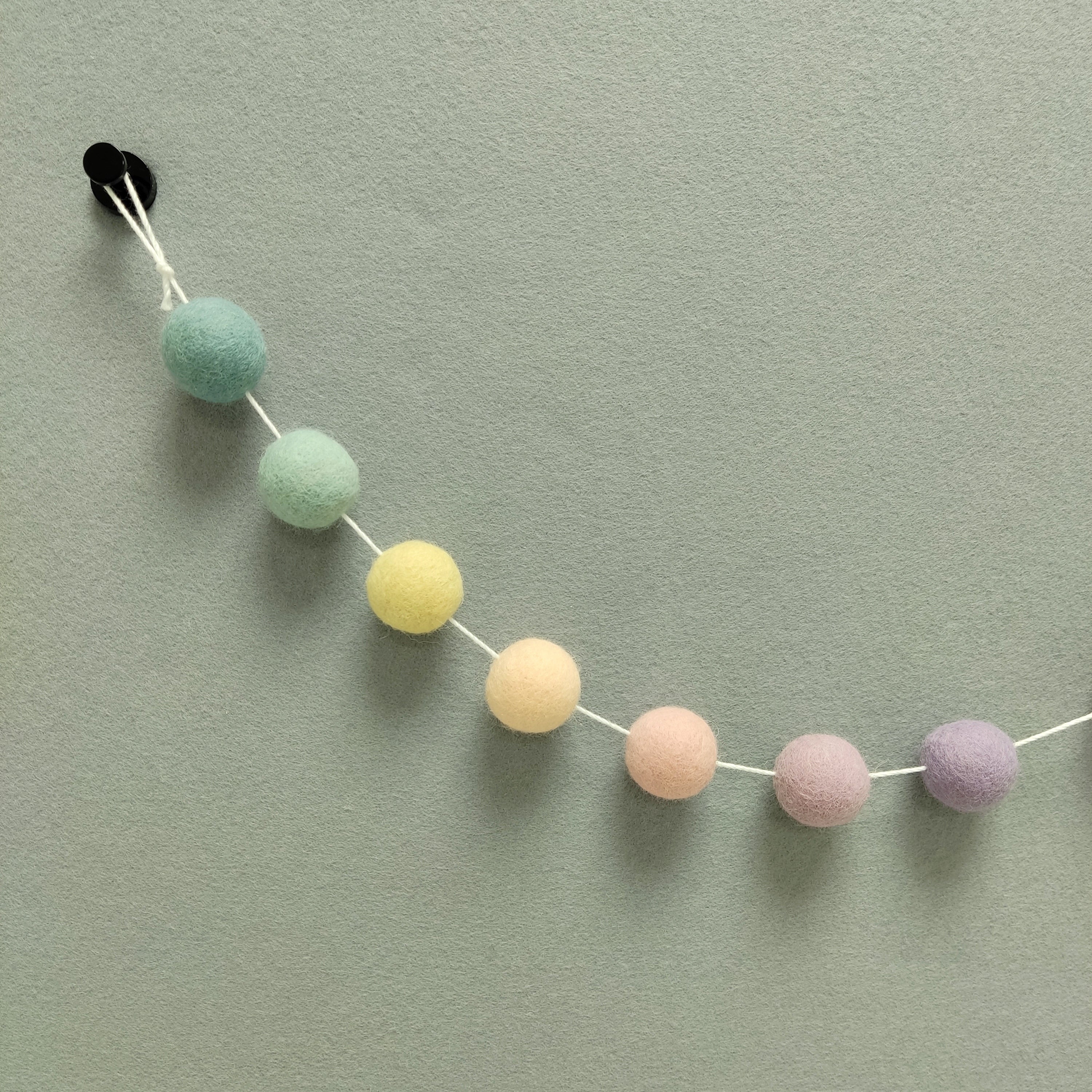 Zoom sur les pompons arc-en-ciel pastel beige rosé, rose poudré, jaune vanille, vert céladon, bleu nordique, lilas et mauve