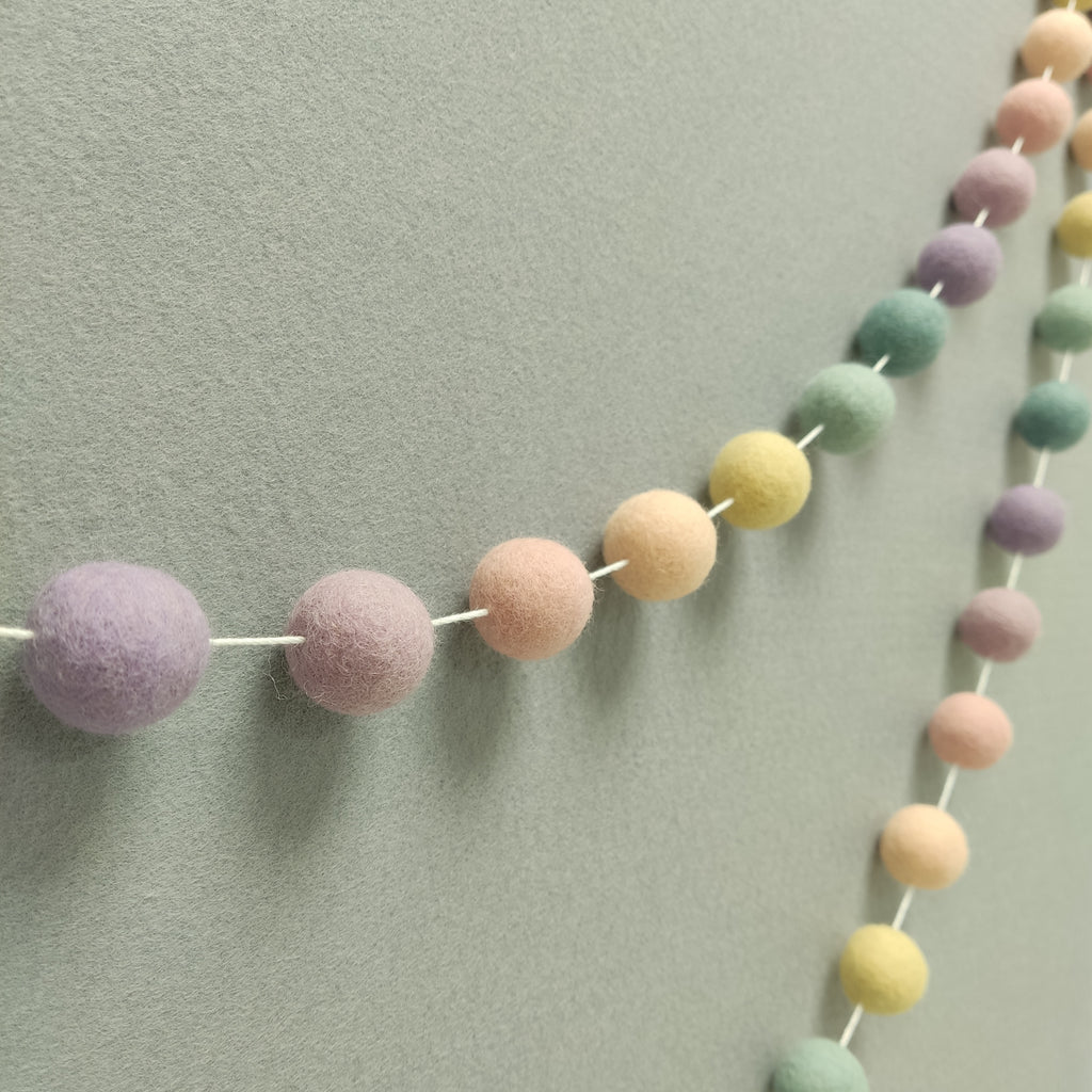 Guirlande en boules de feutre aux teintes pâles arc-en-ciel vue de profil