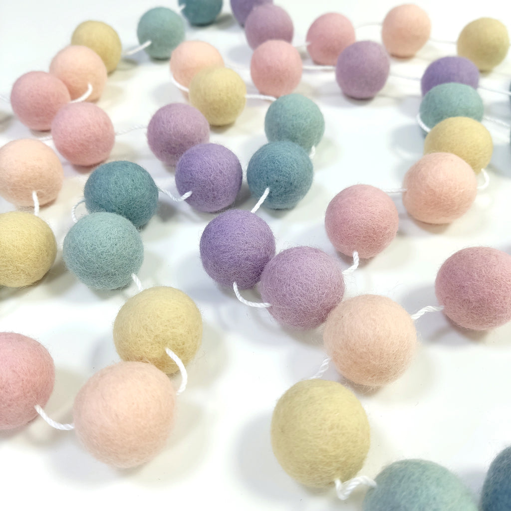 Guirlande de pompons pastels étalée sur une table avec les pompons espacés