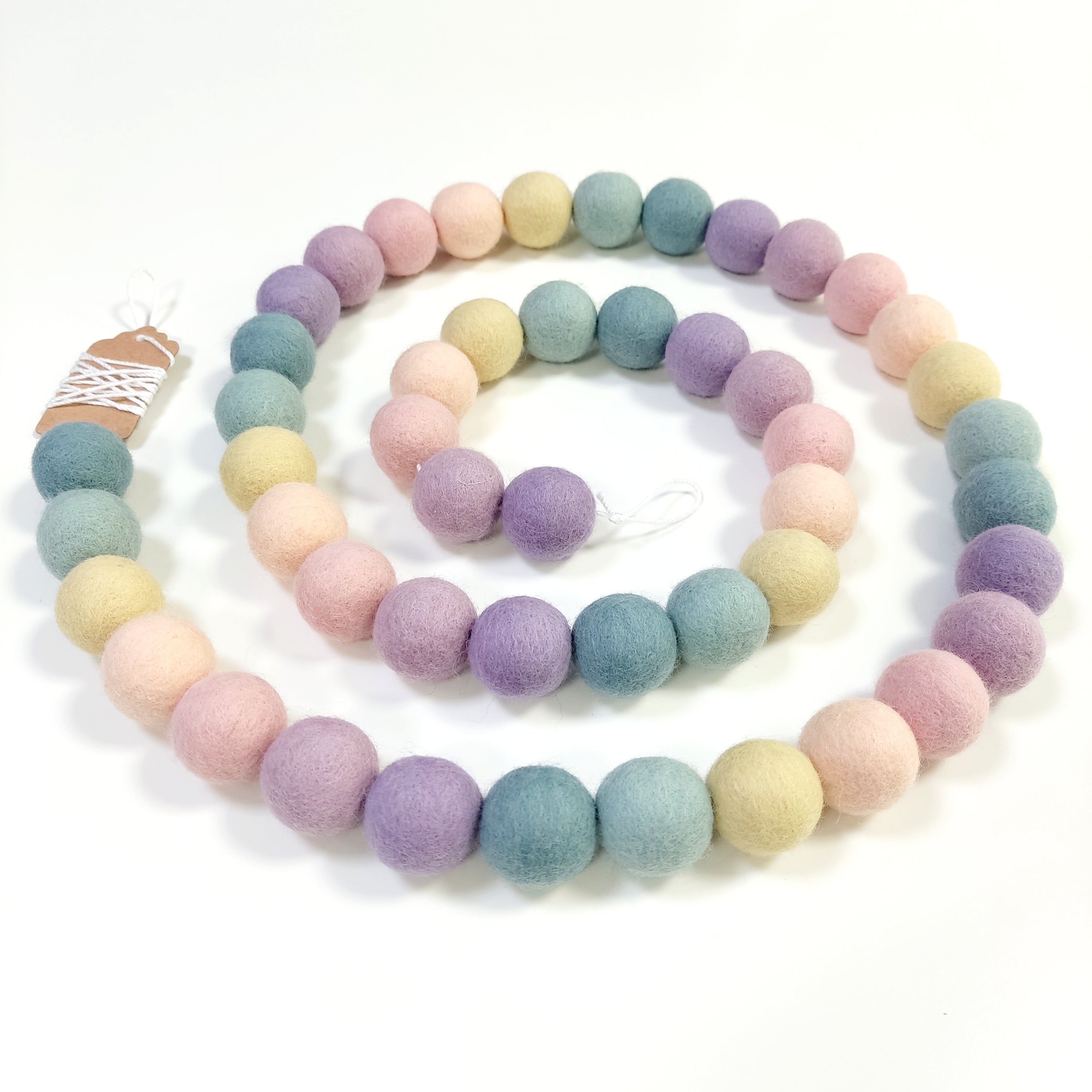 Guirlande de boules de laine feutrée aux couleurs en dégradé arc-en-ciel pastel disposée en spirale vue de dessus
