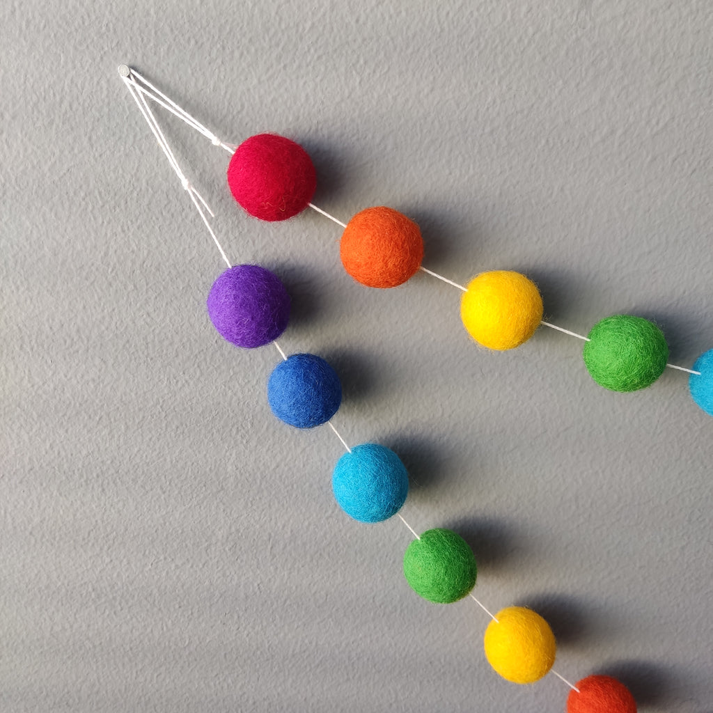 Détails de l'accrochage de la guirlande de pompons feutrés arc-en-ciel intense