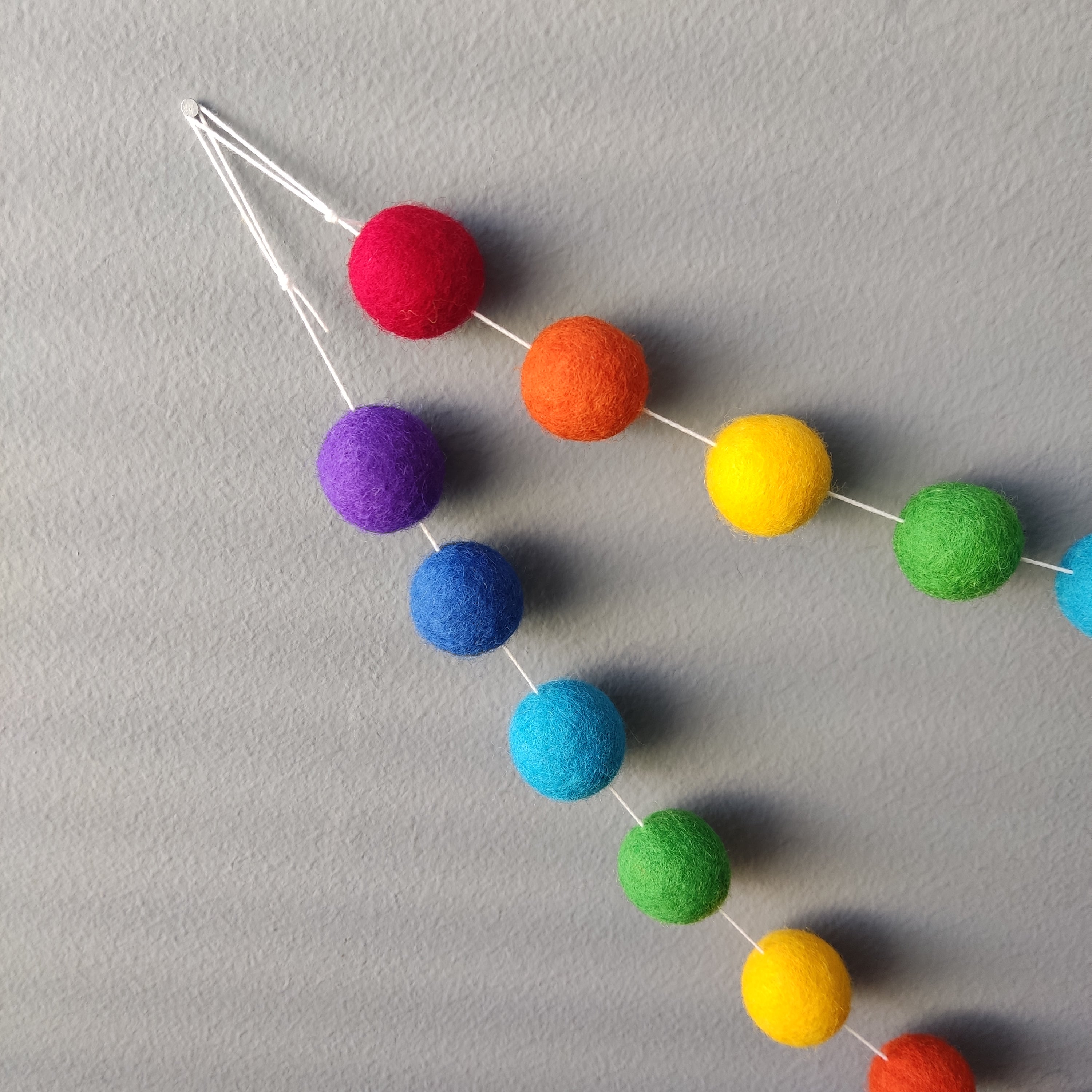 Détails de l'accrochage de la guirlande de pompons feutrés arc-en-ciel intense