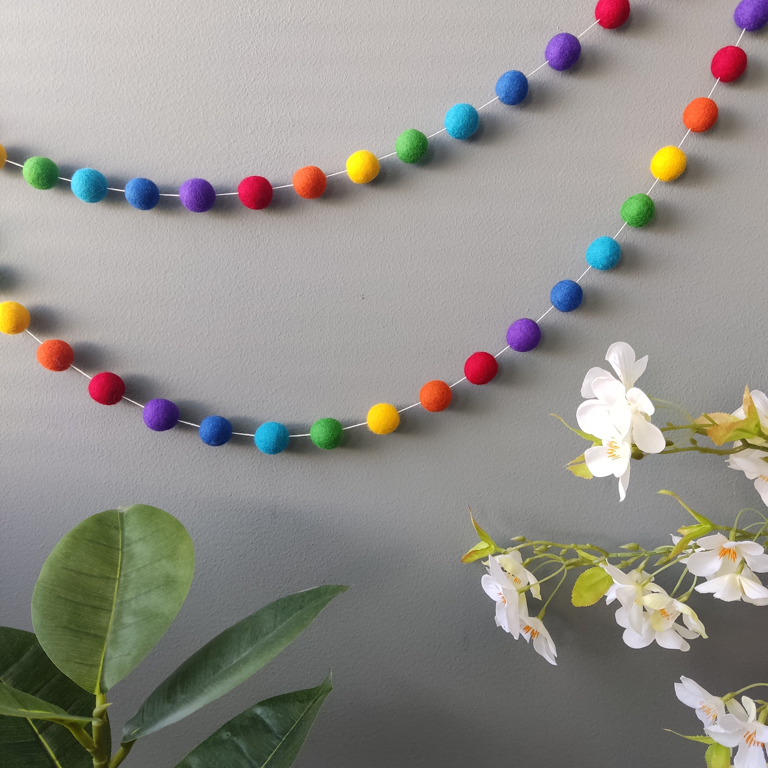 Guirlande en boules de feutre arc-en-ciel aux couleurs vives sur un mur