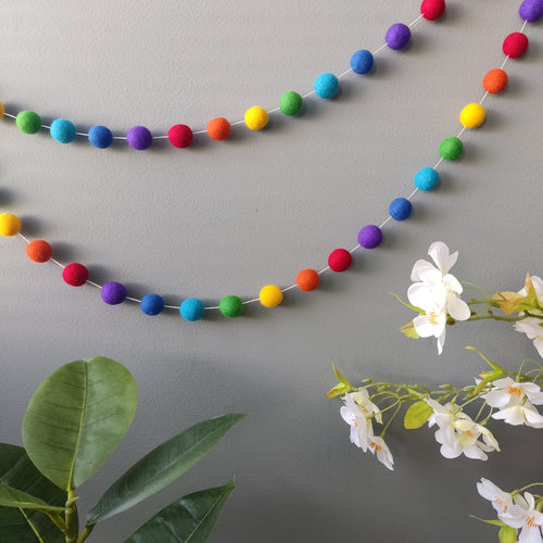 Guirlande en boules de feutre arc-en-ciel aux couleurs vives sur un mur