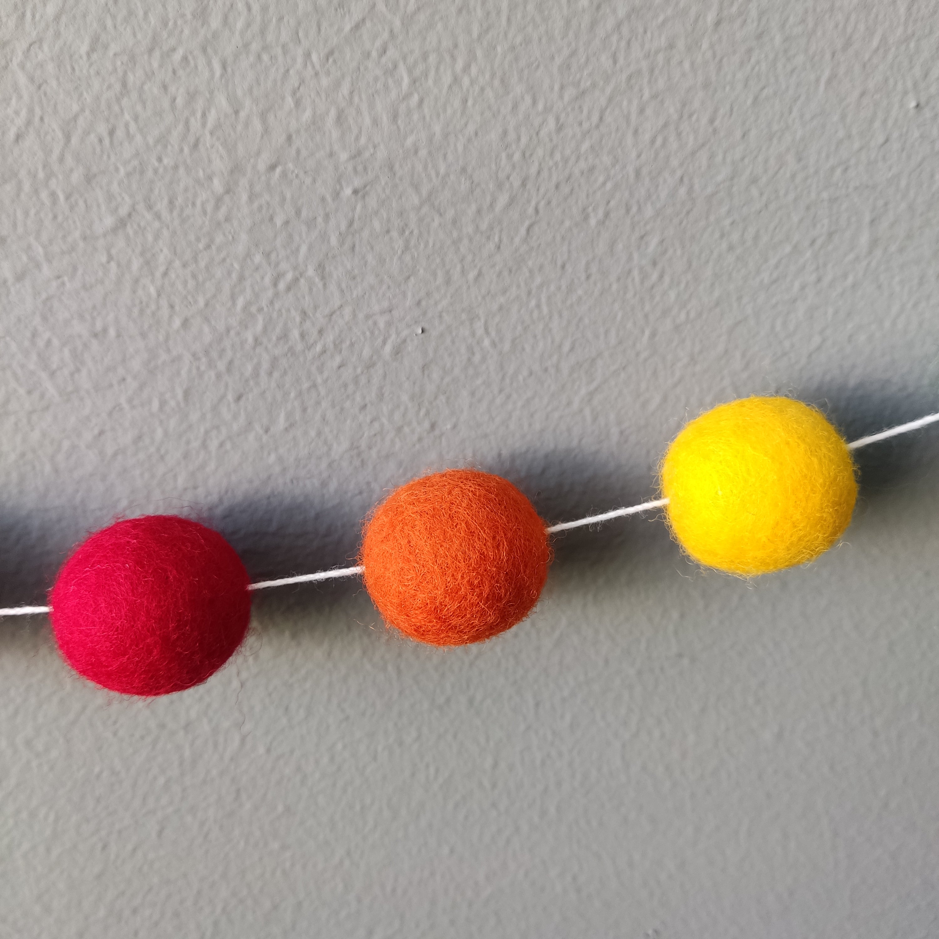 Zoom sur les pompons de feutre rouge orange et jaune de la guirlande arc-en-ciel intense
