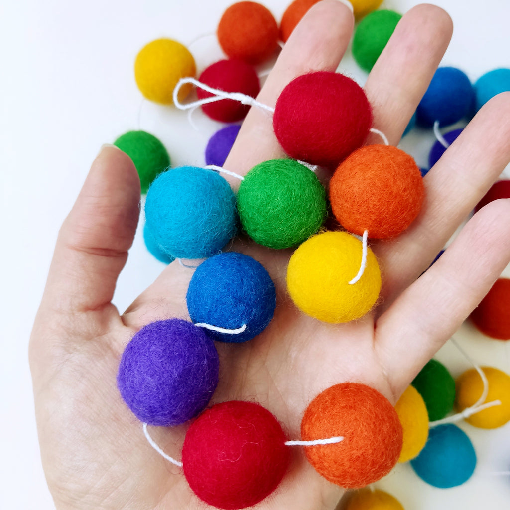 Pompons feutrés de la guirlande arc-en-ciel intense dans une main