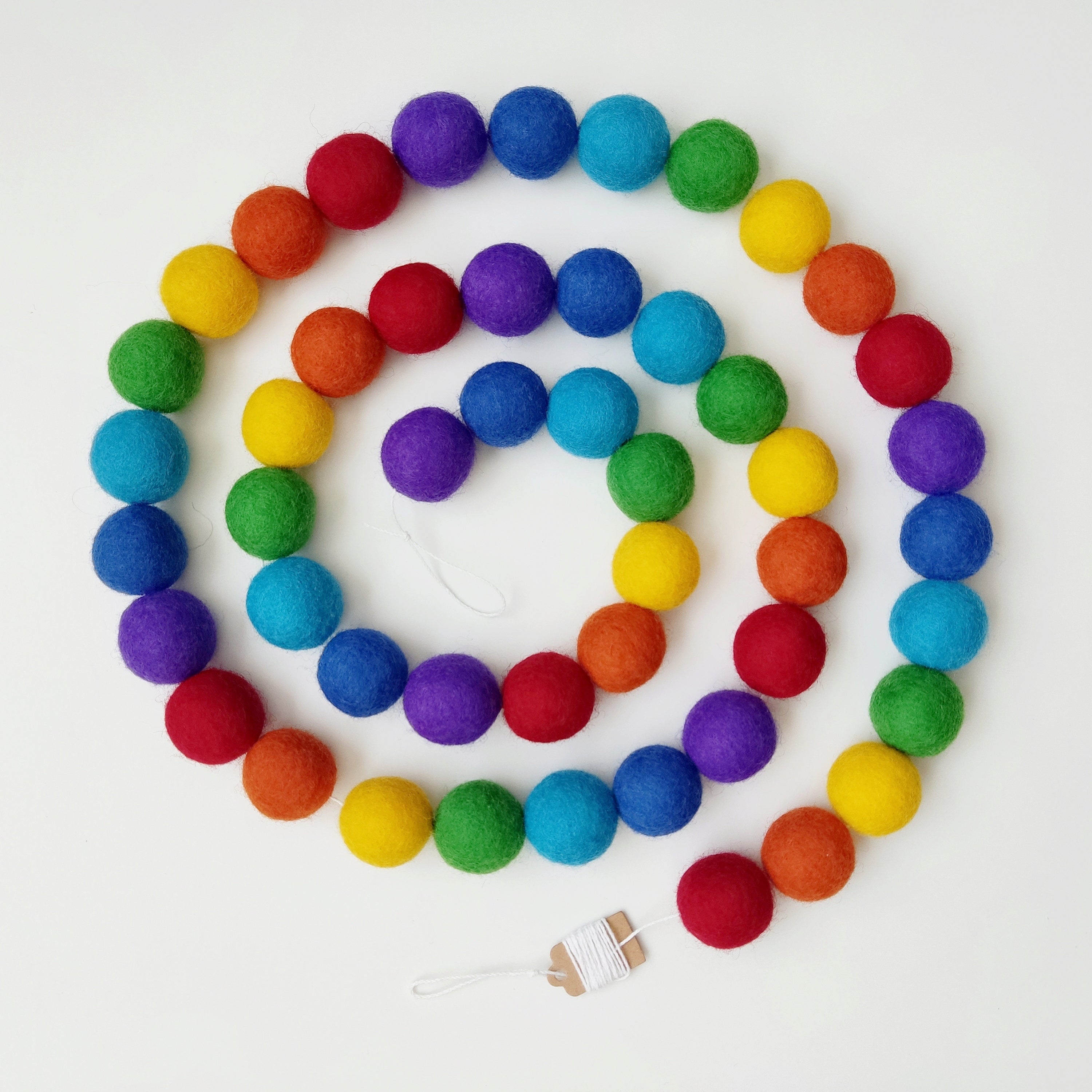 Vue de dessus de la guirlande en boules de feutre arc-en-ciel intense disposée en spirale