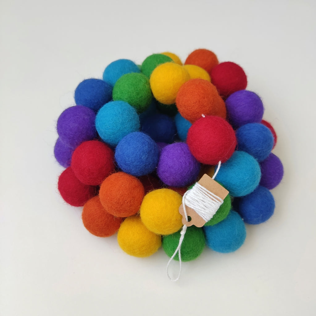 Guirlande arc-en-ciel intense avec les pompons rassemblés sur le fil de coton