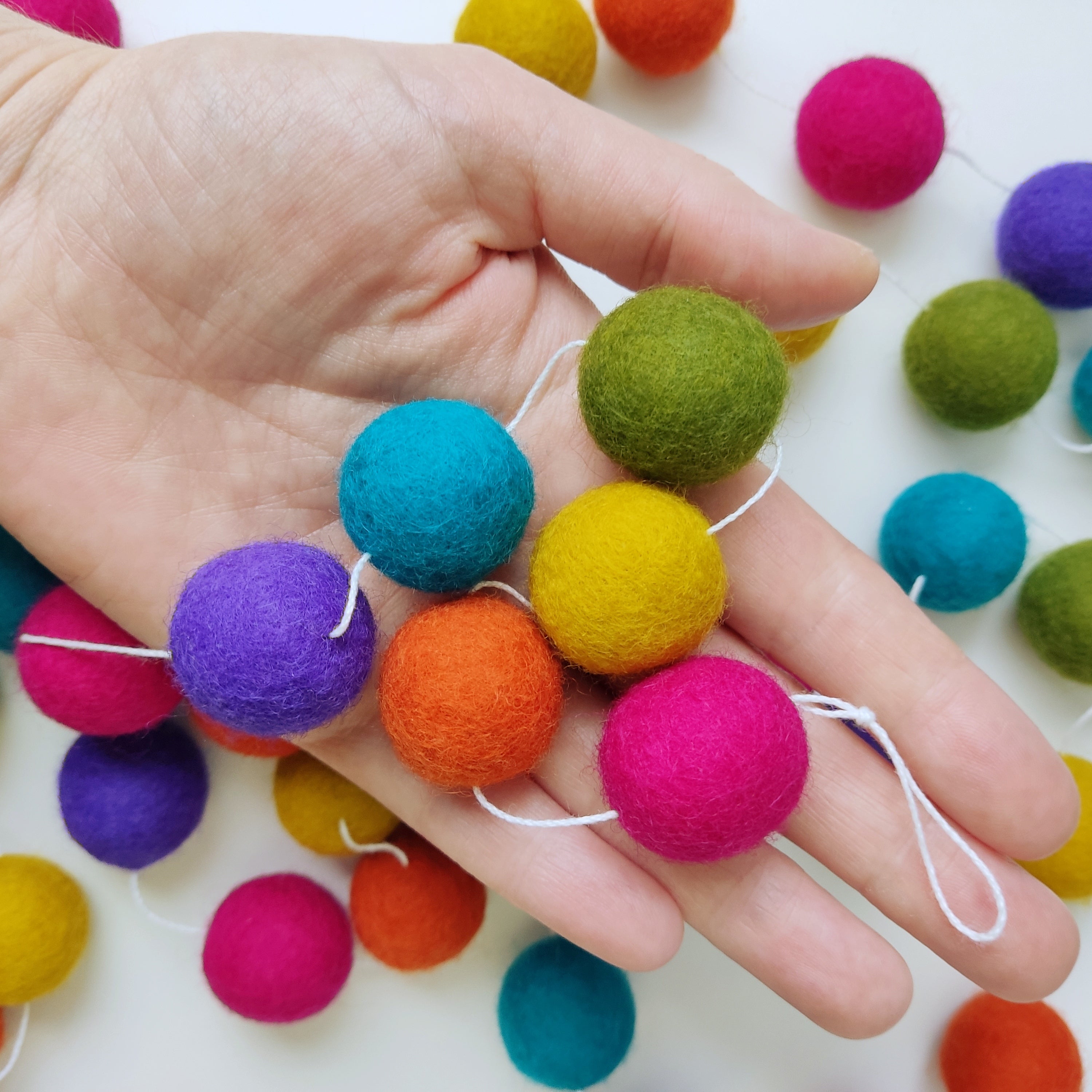 Pompons feutrés rose, orange, jaune, vert, bleu, violet, de la guirlande arc-en-ciel mexicain dans une main