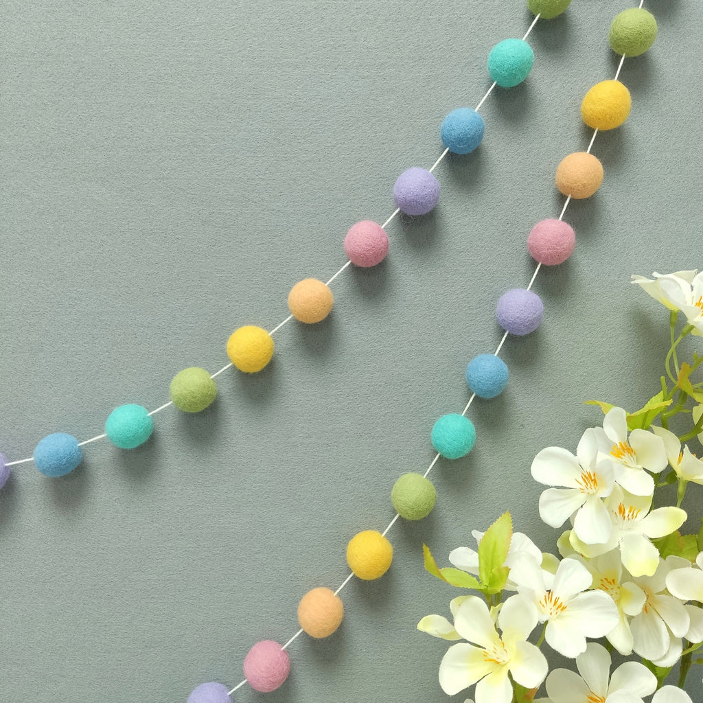 Guirlande de pompons feutrés arc-en-ciel pastel accrochée au mur