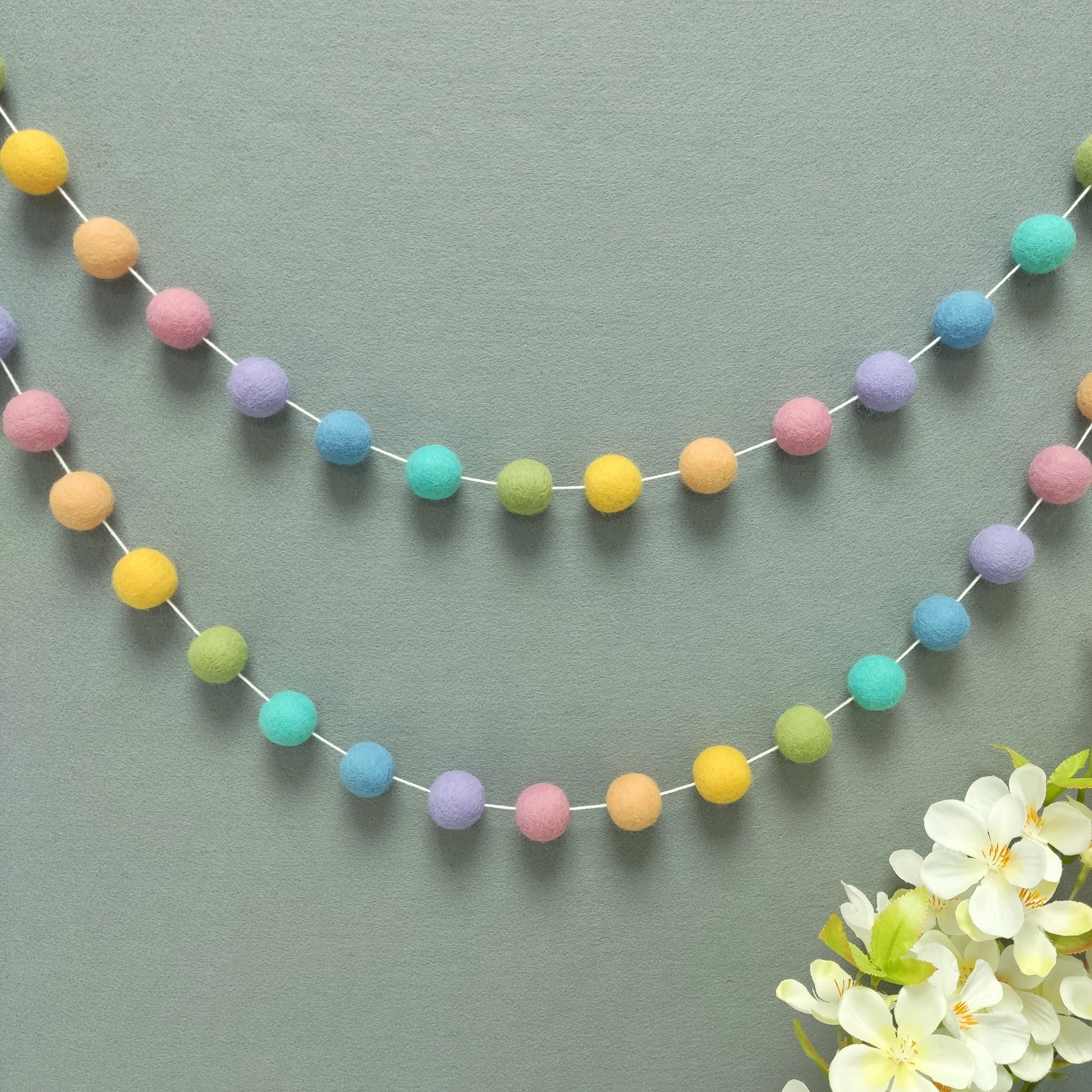 Guirlande de pompons feutrés arc-en-ciel féerique pour mur de chambre d'enfant ou fille, vue de loin