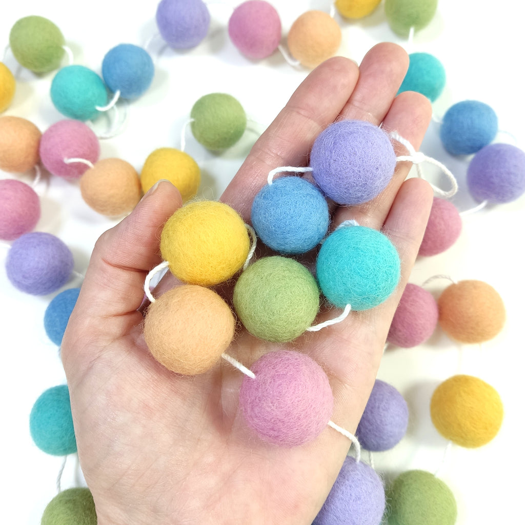 Détails des pompons en laine feutrés arc-en-ciel pastel dans une main