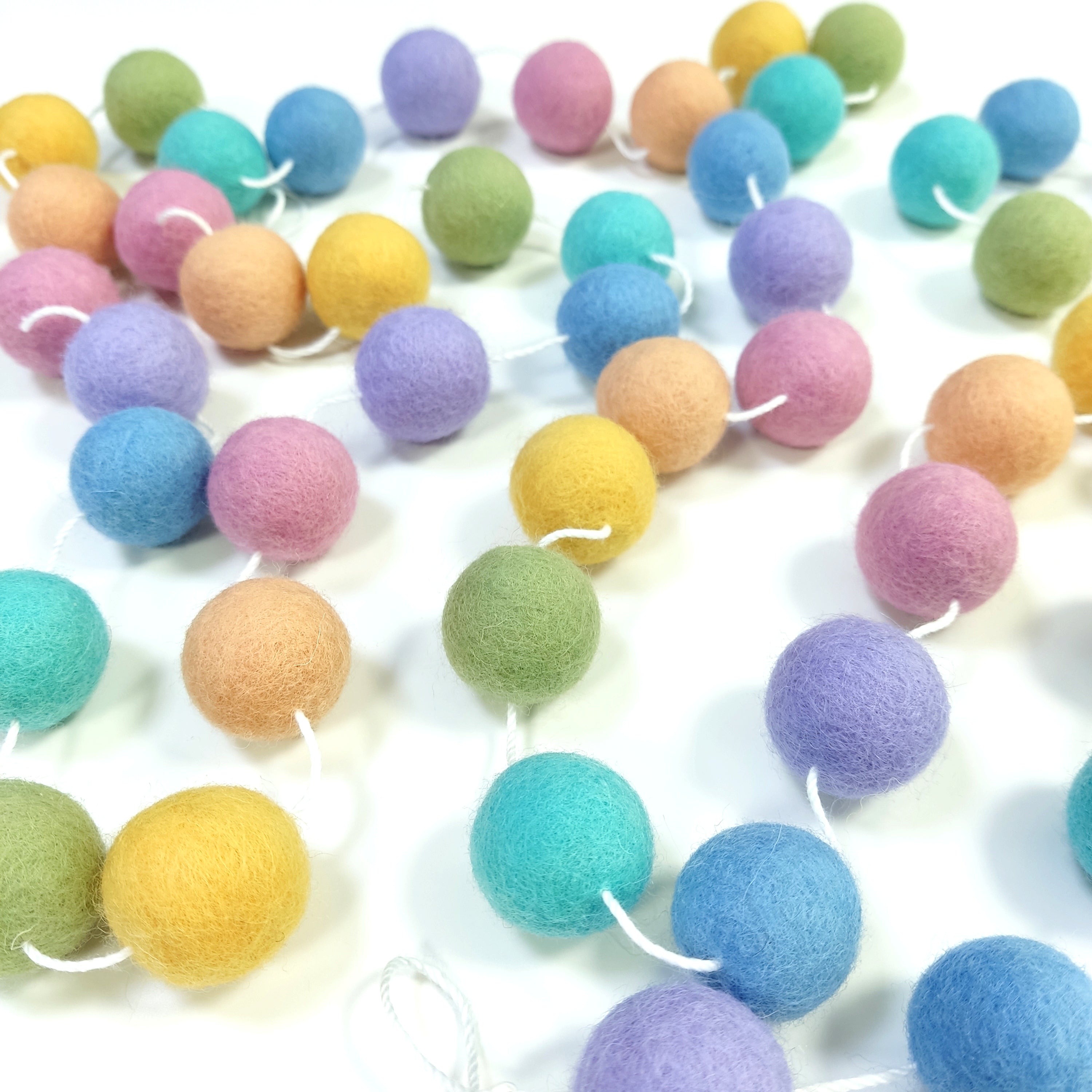 Guirlande en pompons de feutre pastel étalée sur une une table avec les pompons espacés