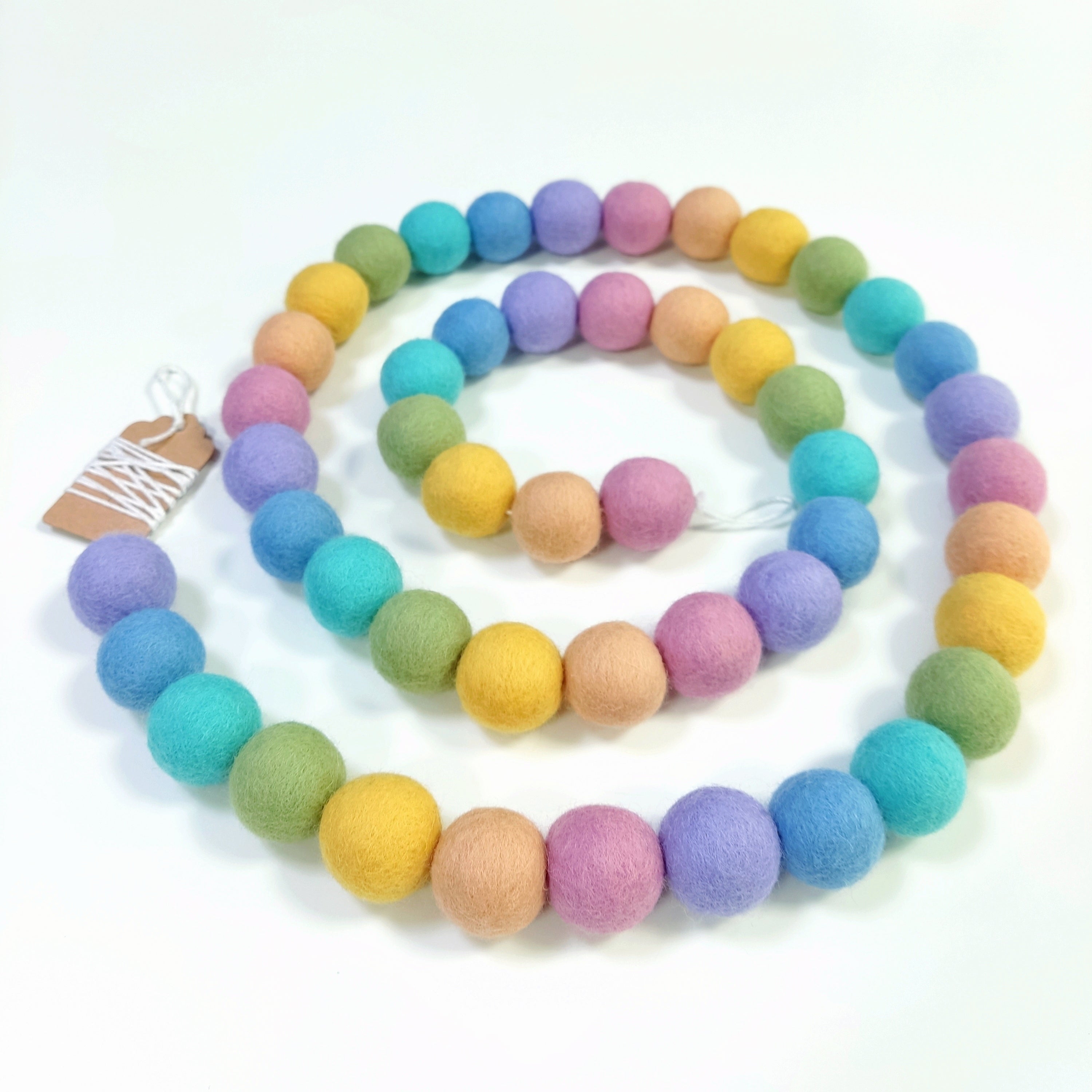 Guirlande arc-en-ciel pastel avec pompons rassemblés sur le fil et posée en spirale sur une table, vue de dessus