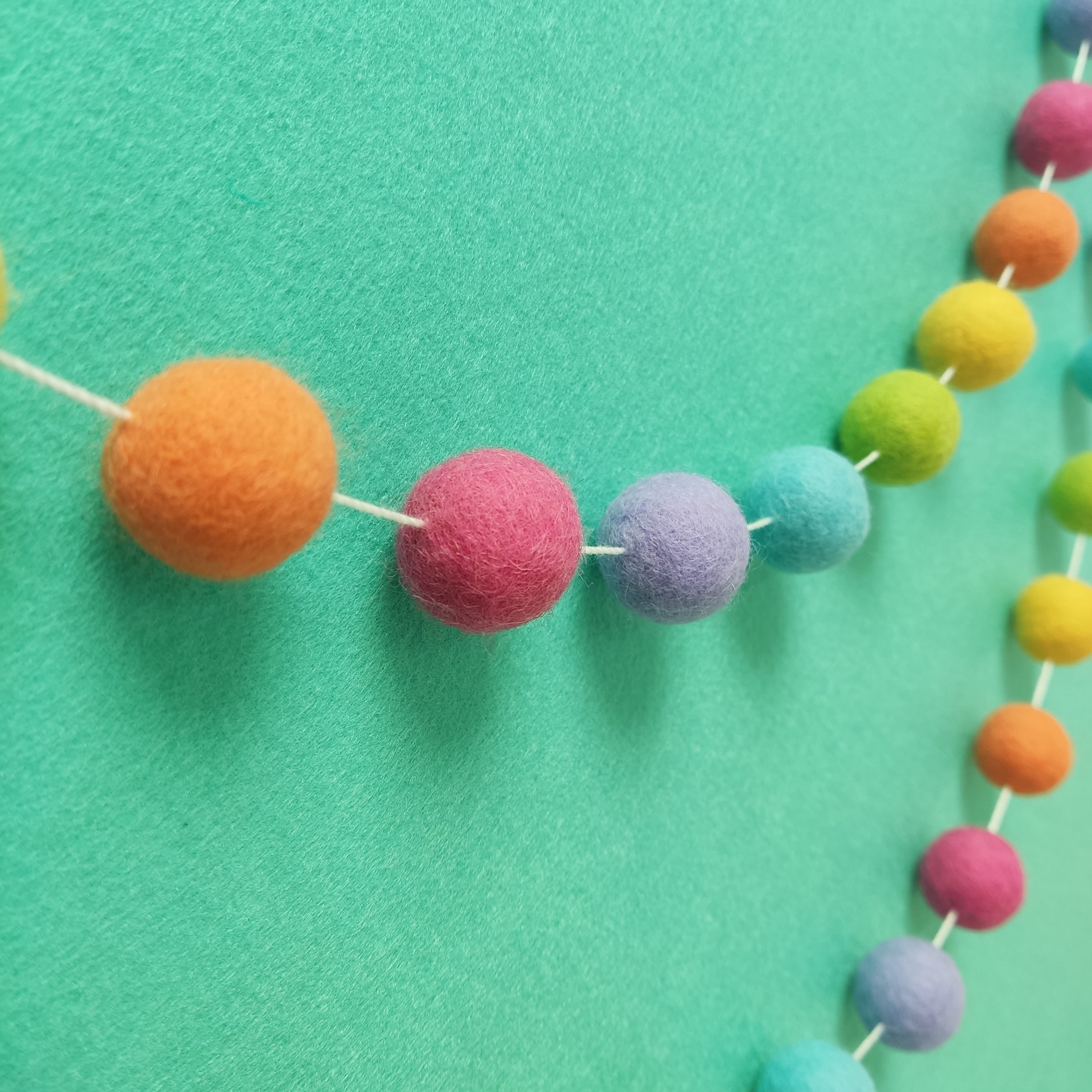 Guirlande arc-en-ciel avec pompons feutrés rose, orange, jaune, vert, bleu, lavande, fixée au mur