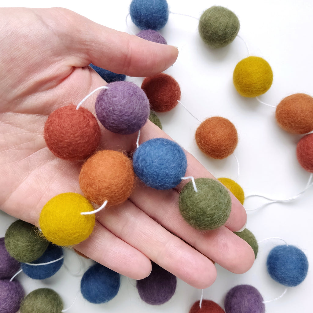 Zoom des pompons de la guirlande arc-en-ciel vintage dans une main pour visualiser la taille des pompons