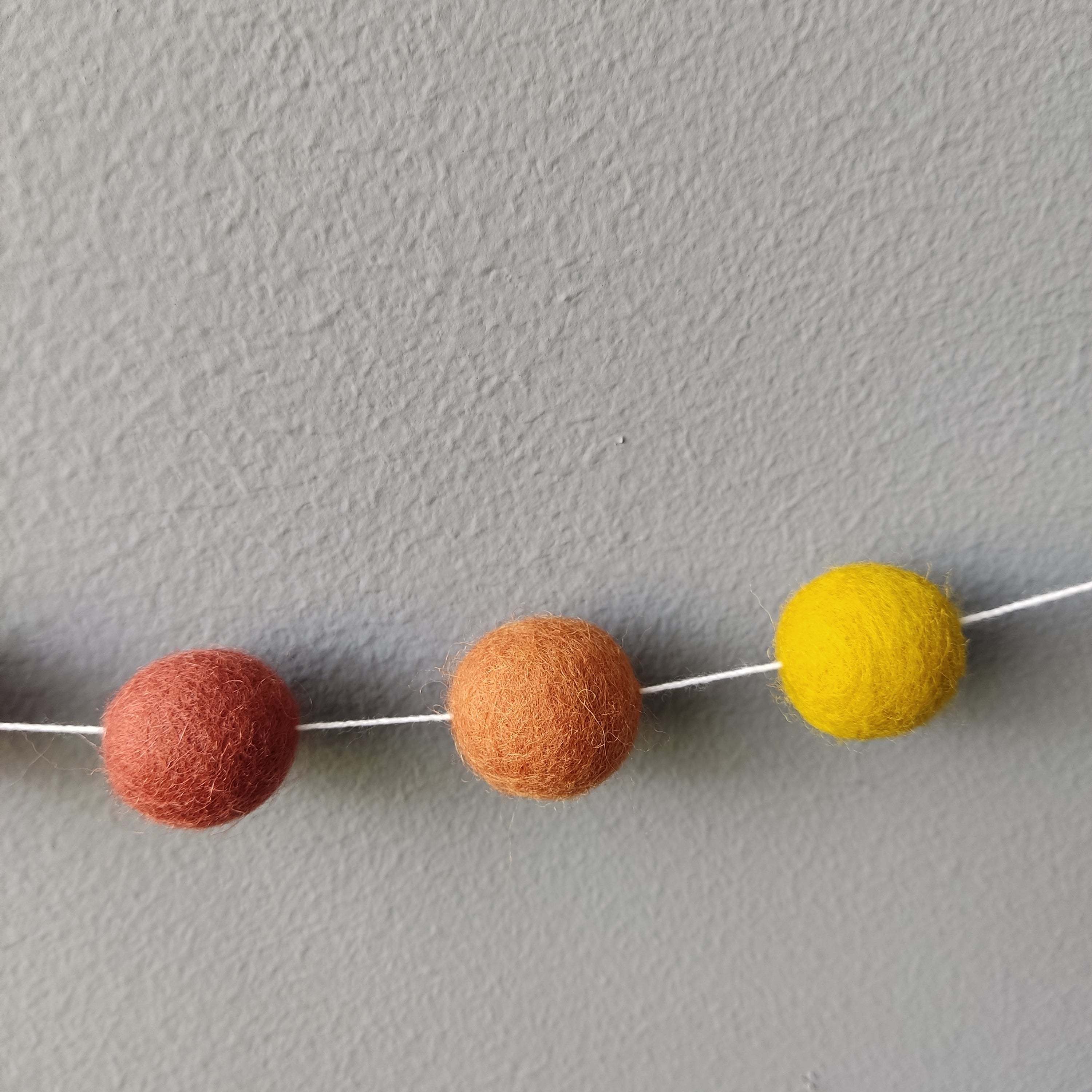 Zoom des pompons sur le fil pour les couleurs terracotta rouge, terracotta cuivre et jaune moutarde