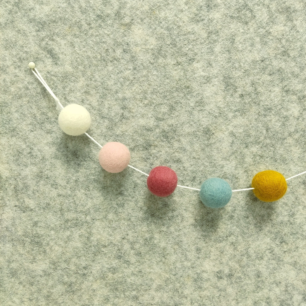Détail des 5 couleurs de pompons feutrés blanc, ocre doré, bleu nordique, rose poudré et rose boisé