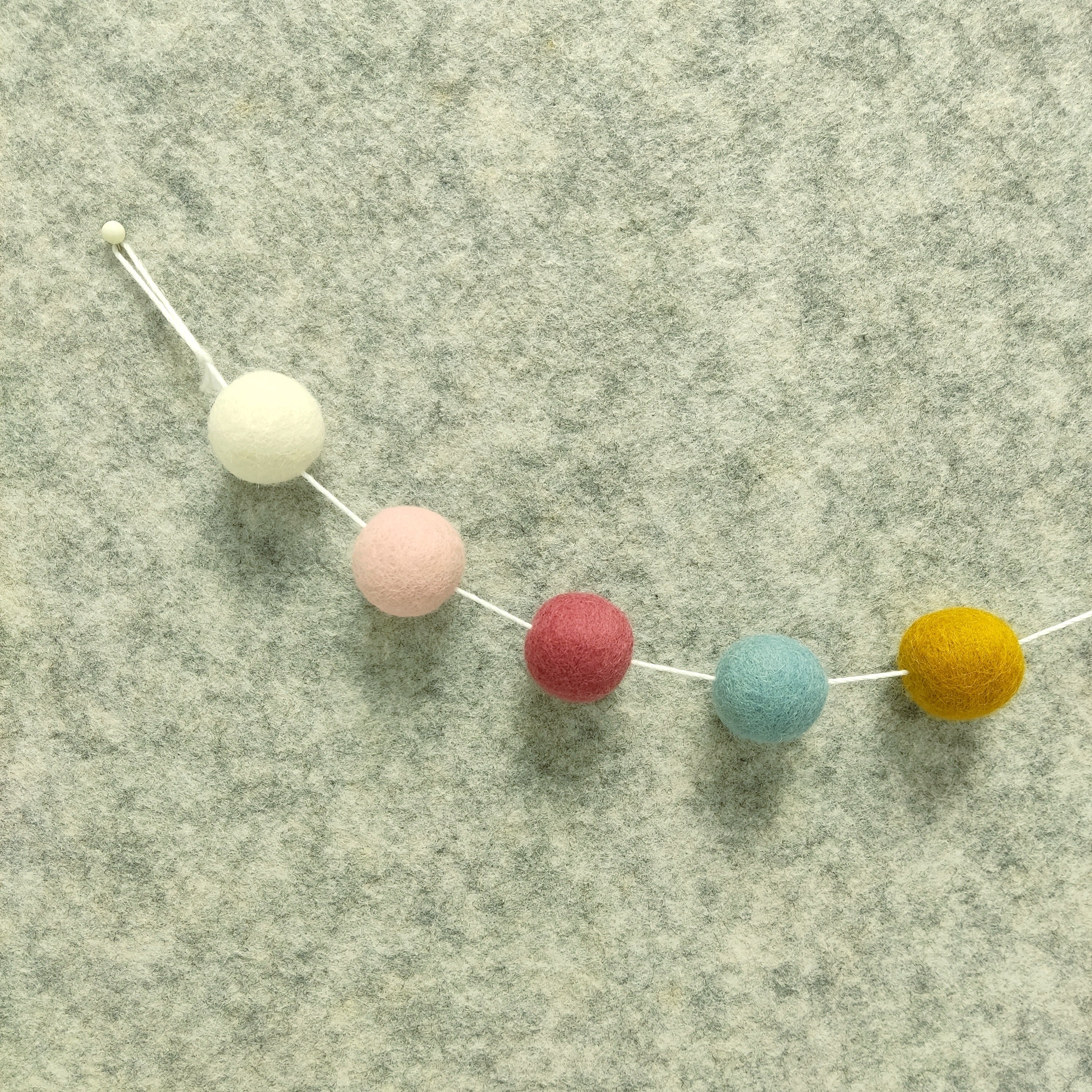 Détail des 5 couleurs de pompons feutrés blanc, ocre doré, bleu nordique, rose poudré et rose boisé