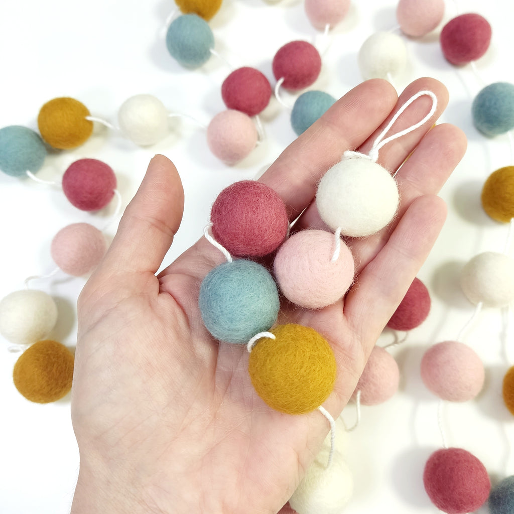 Zoom sur les pompons en laine mérinos aube scandinave dans une main, teintes douces et nordiques