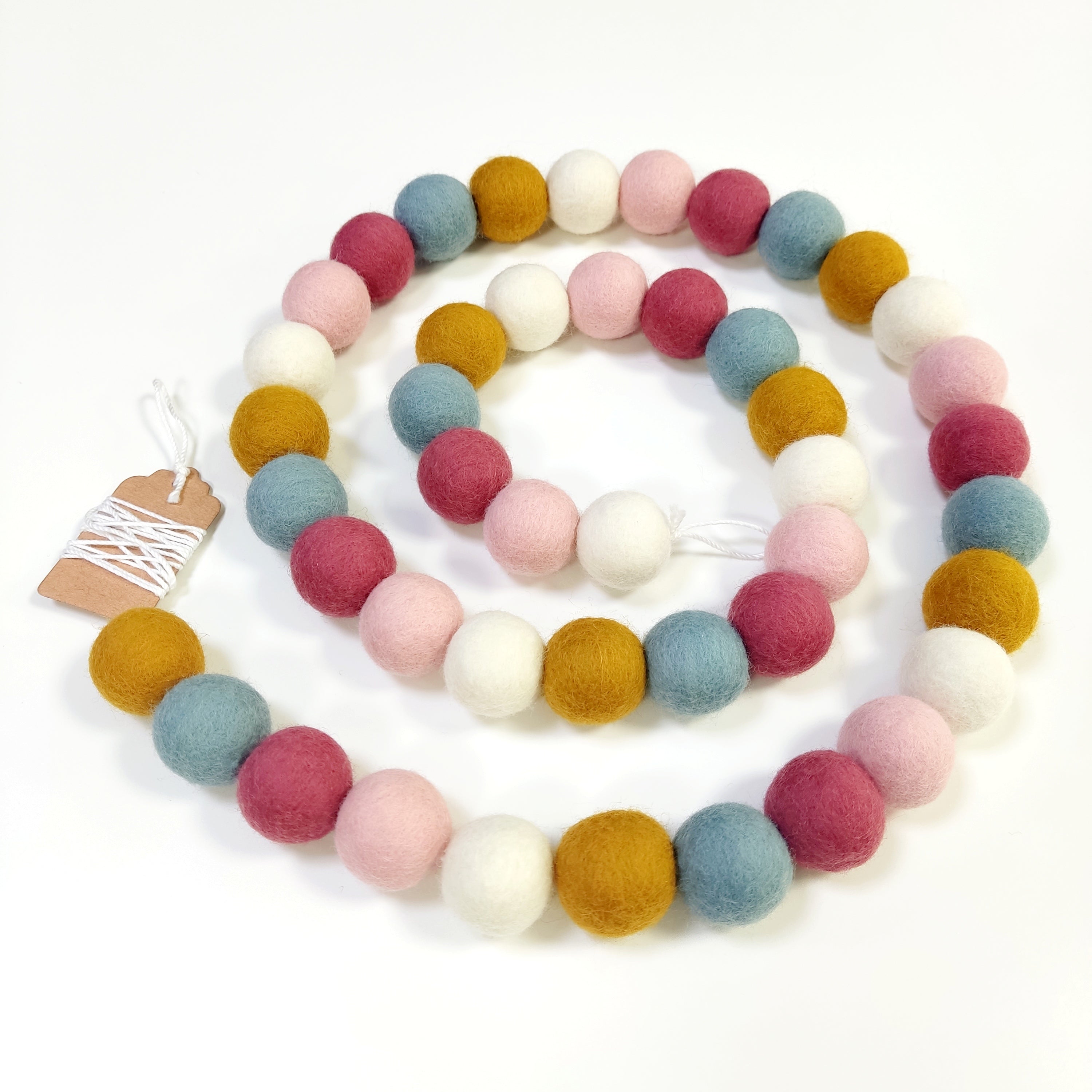 Guirlande de pompons feutrés aube scandinave disposée en spirale sur fond blanc