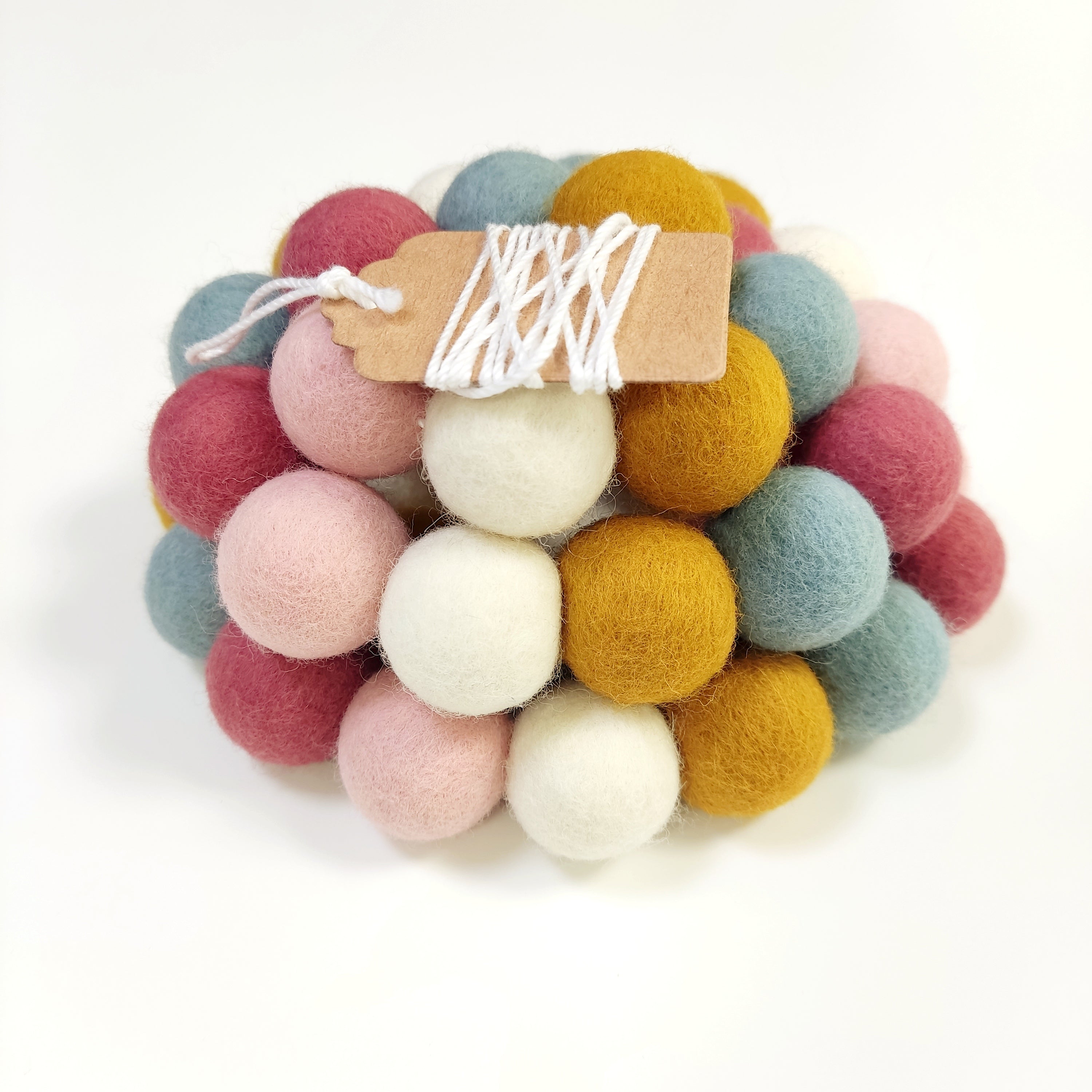 Zoom sur la guirlande de pompons en laine mérinos aube scandinave avec étiquette CELAINEDECO