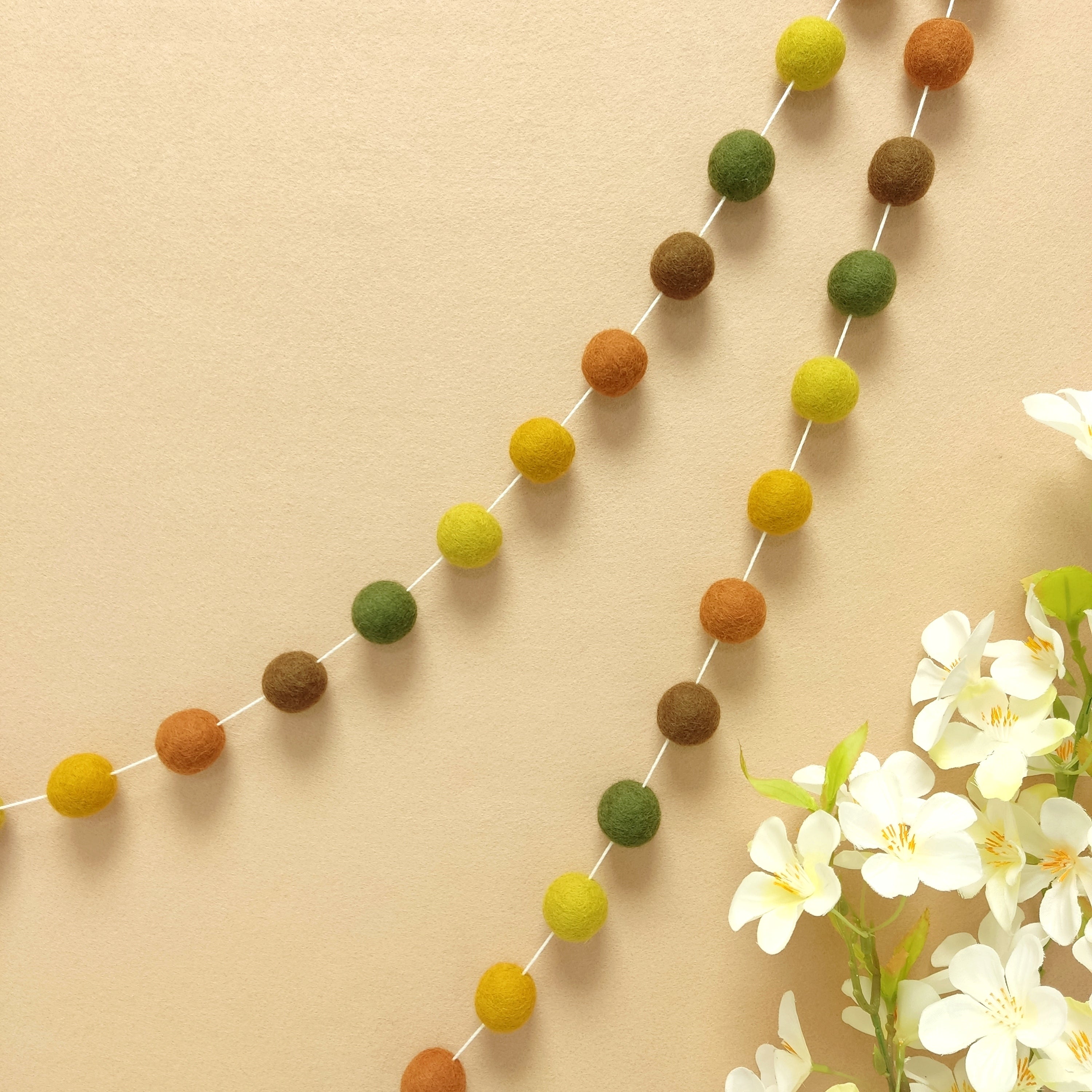 Guirlande murale de pompons feutrés aux teintes d'automne accrochée sur un mur vue de près