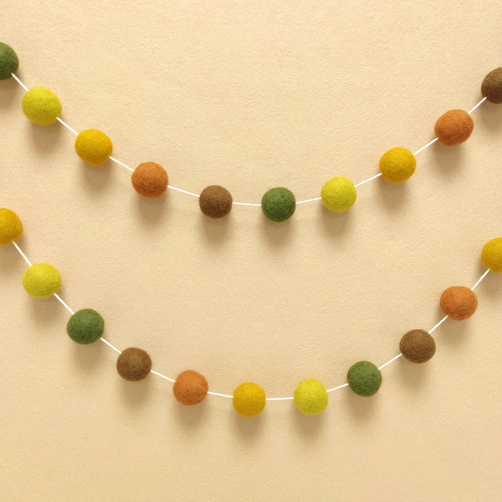 Guirlande de pompons feutrés automne suspendue sur un mur de chambre en arc de cercle