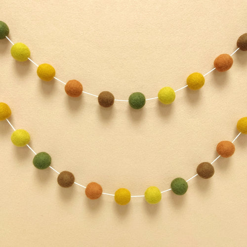 Guirlande de pompons feutrés automne suspendue sur un mur de chambre en arc de cercle