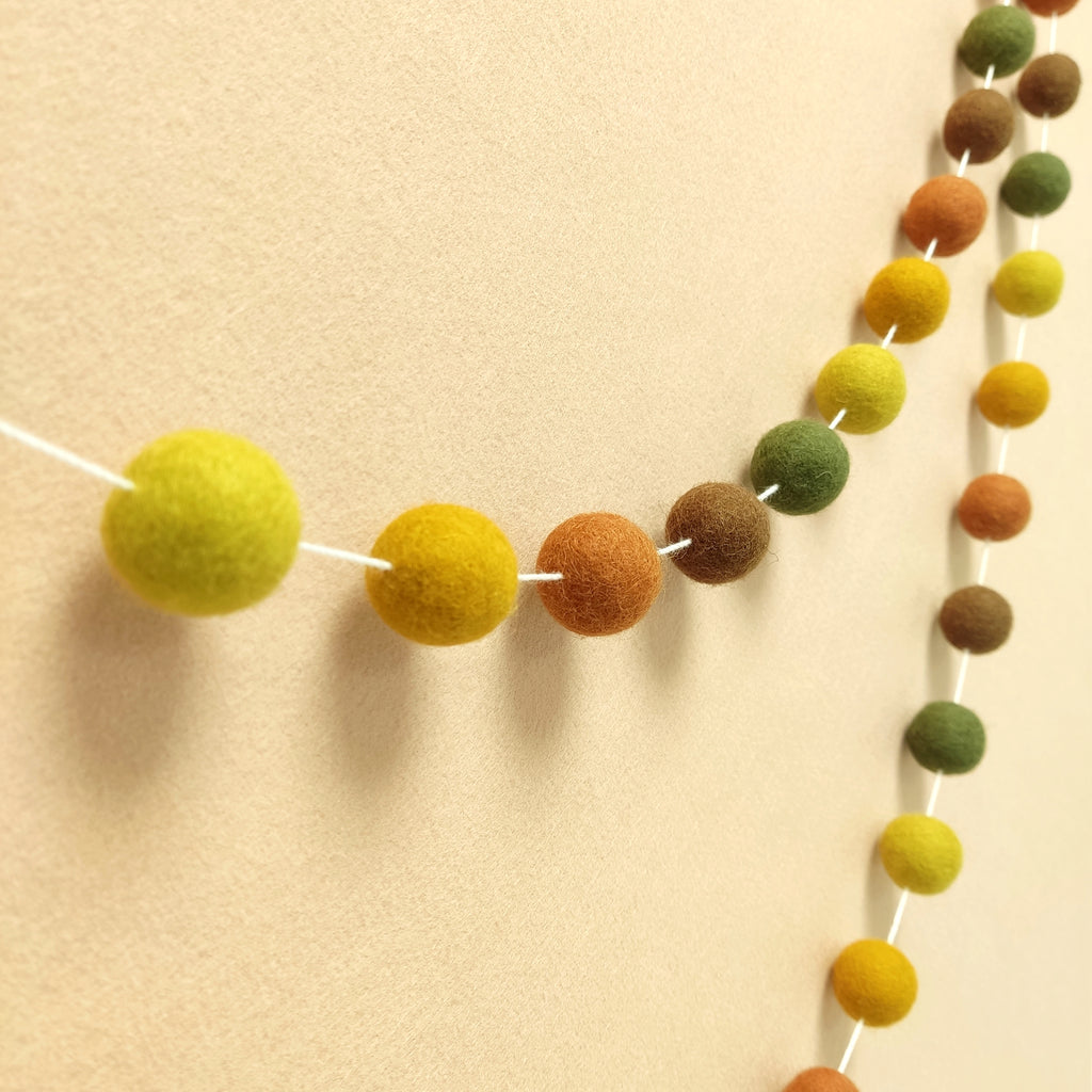 Guirlande en boules de feutre teintes marrons ocre rouille vert vue de profil sur un mur