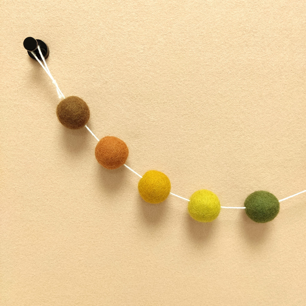 Détails de pompons terracotta cuivre, jaune chargreuse, vert olive, brun noisette et ocre doré de la guirlande automne