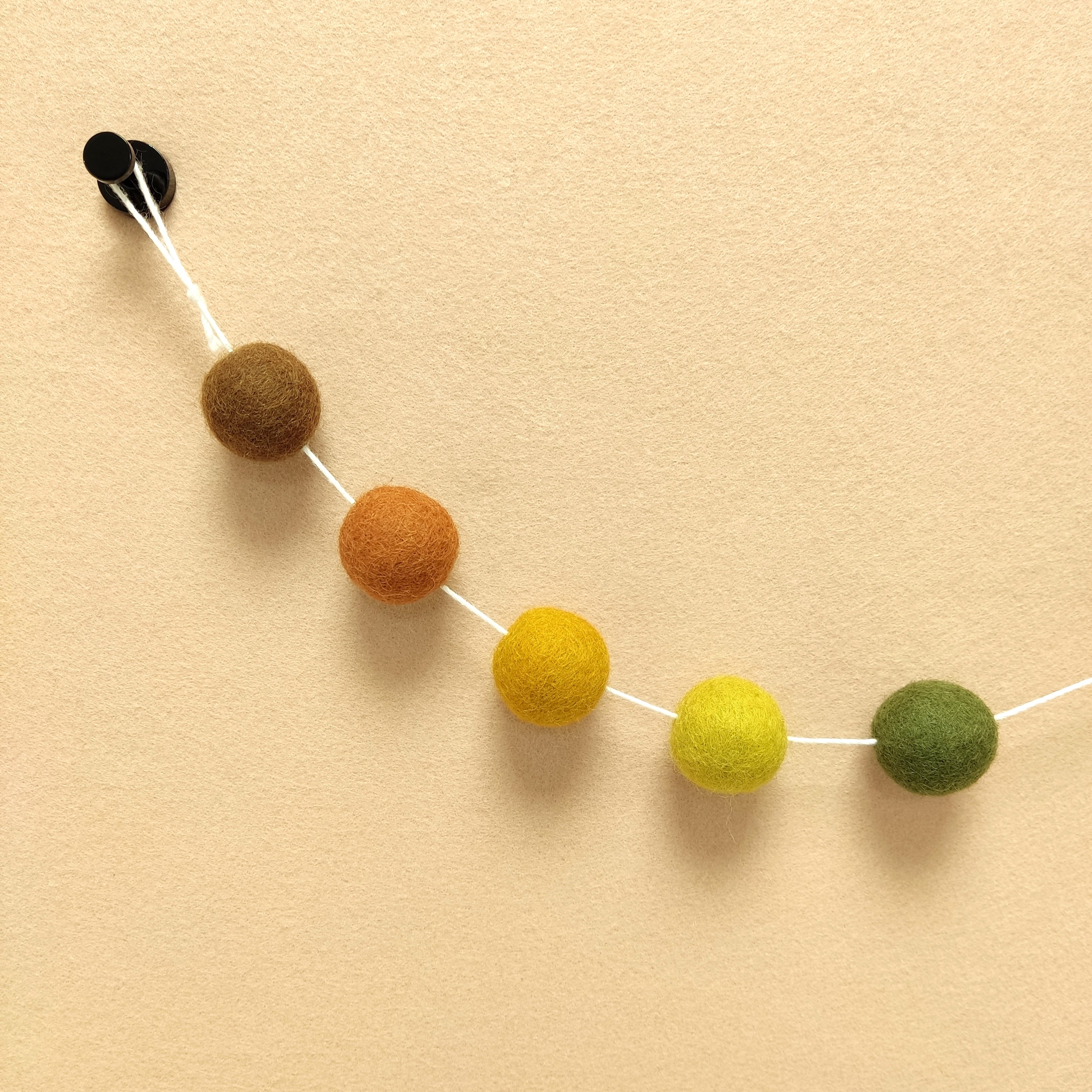 Détails de pompons terracotta cuivre, jaune chargreuse, vert olive, brun noisette et ocre doré de la guirlande automne