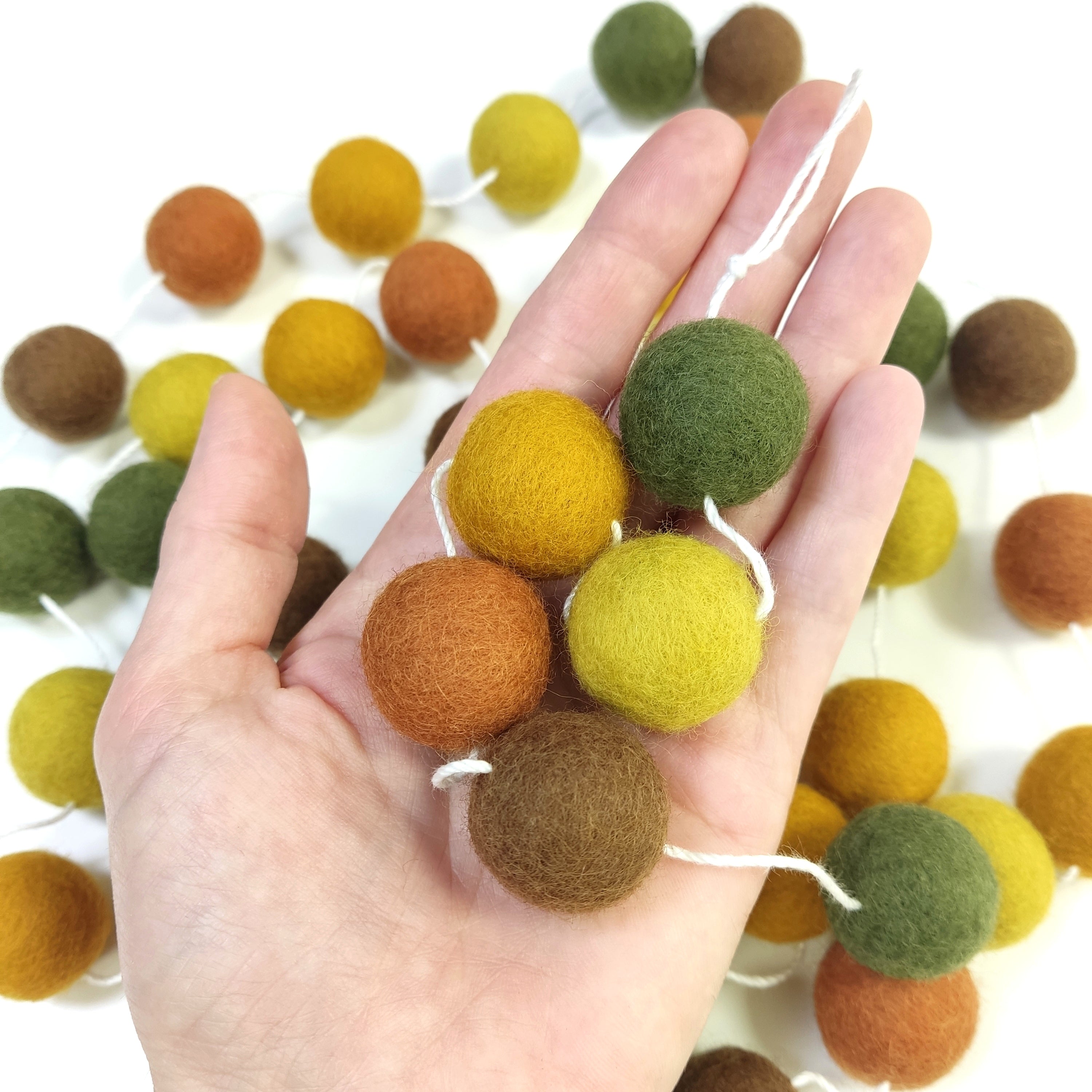 Zoom sur les pompons de 2,5 cm de la guirlande automne dans une main