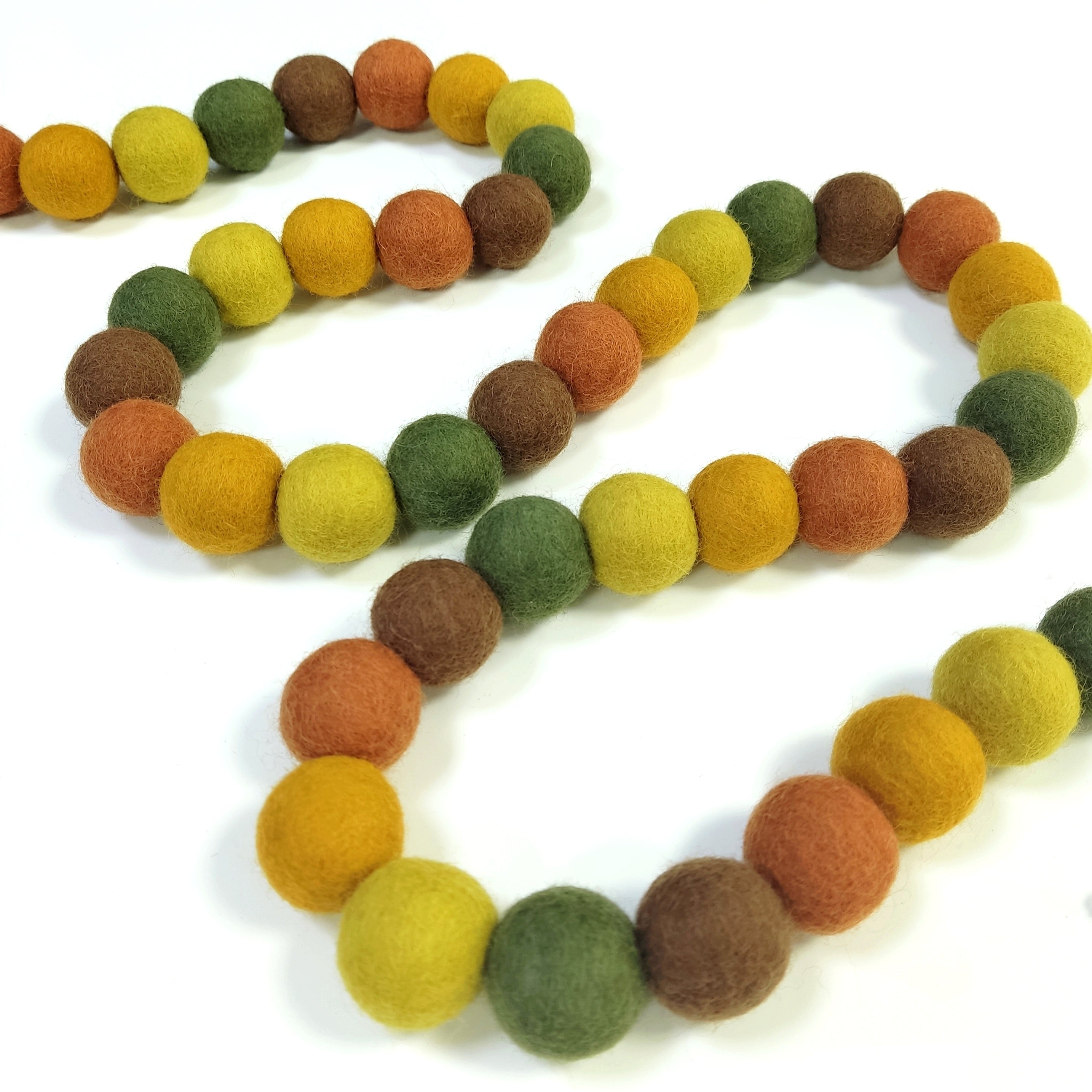 Guirlande en pompons feutrés automne disposée en serpentin sur une table