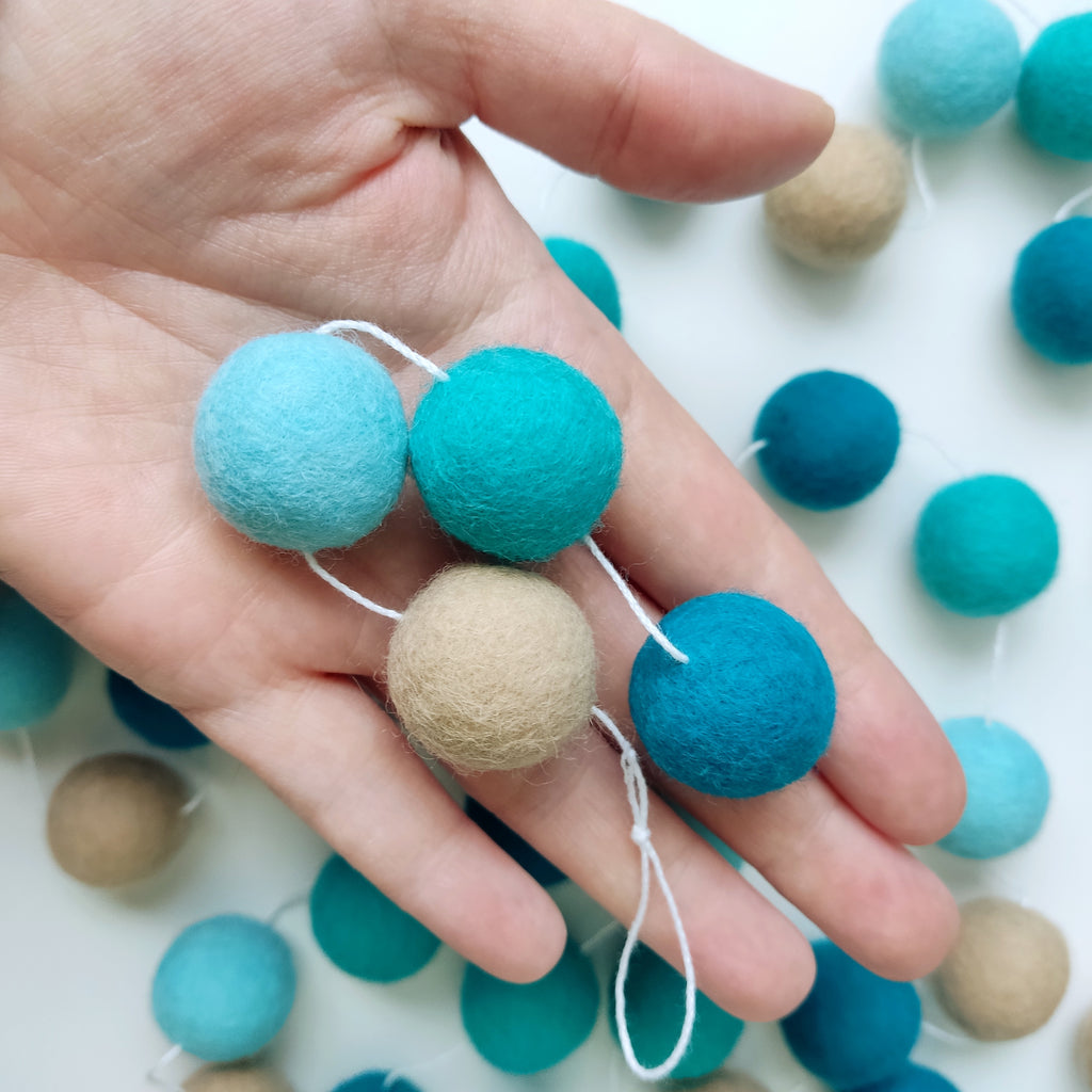 Détails des pompons de 2,5 cm dans une main de la guirlande turquoise beige