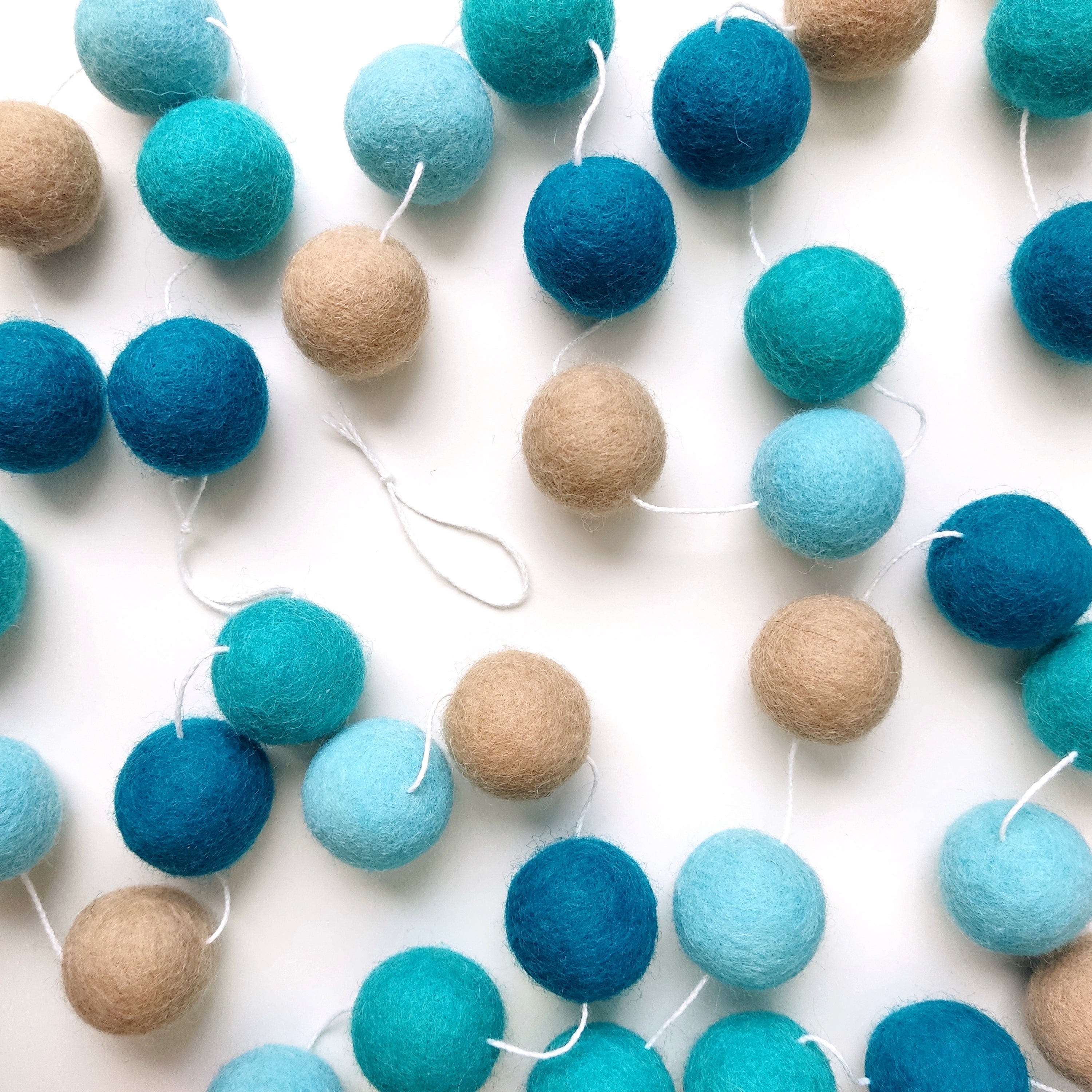 Guirlande de boules feutrées turquoise beige posée sur une table