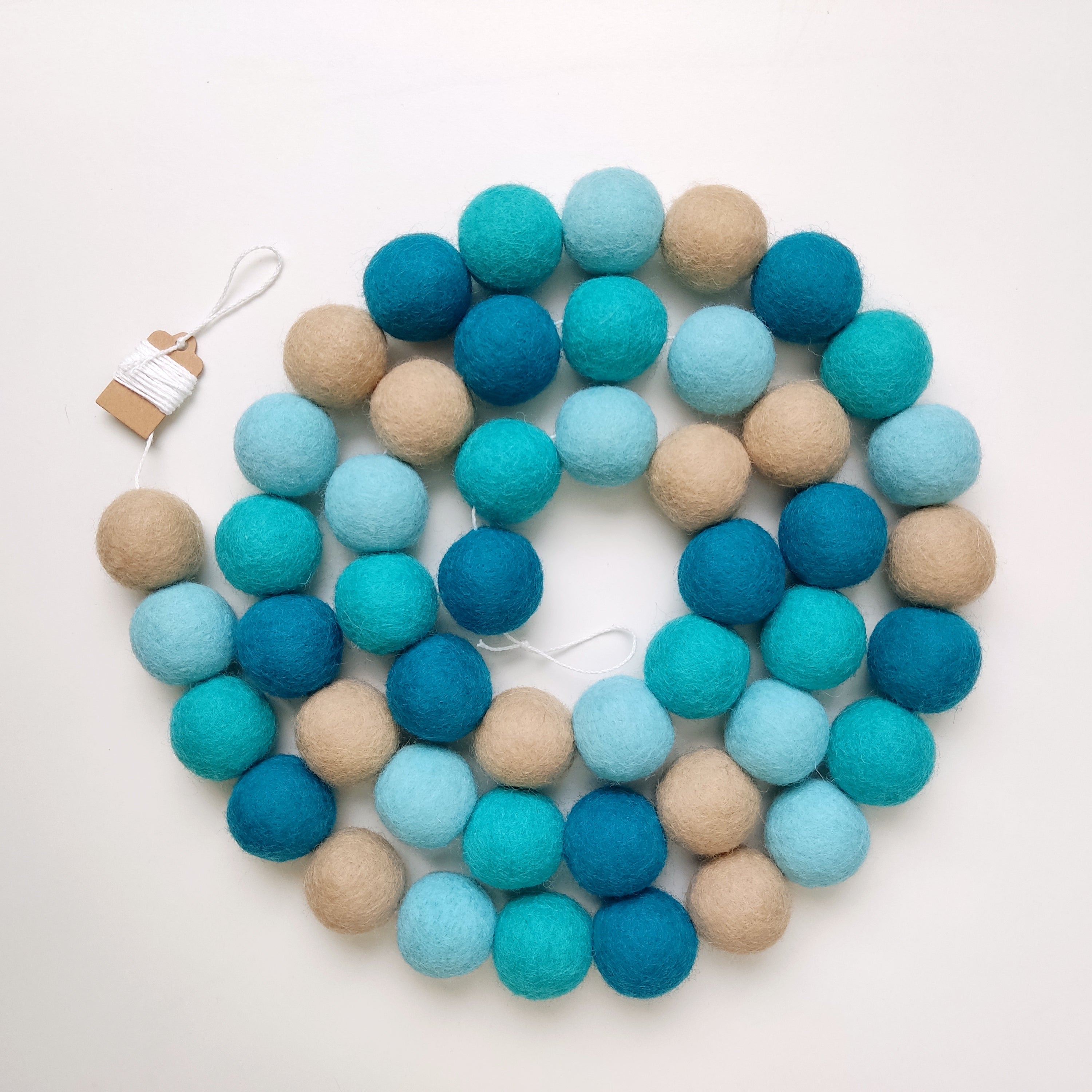 Guirlande pompons bleu turquoise et beige en laine mérinos posée en forme de spirale vue de dessus