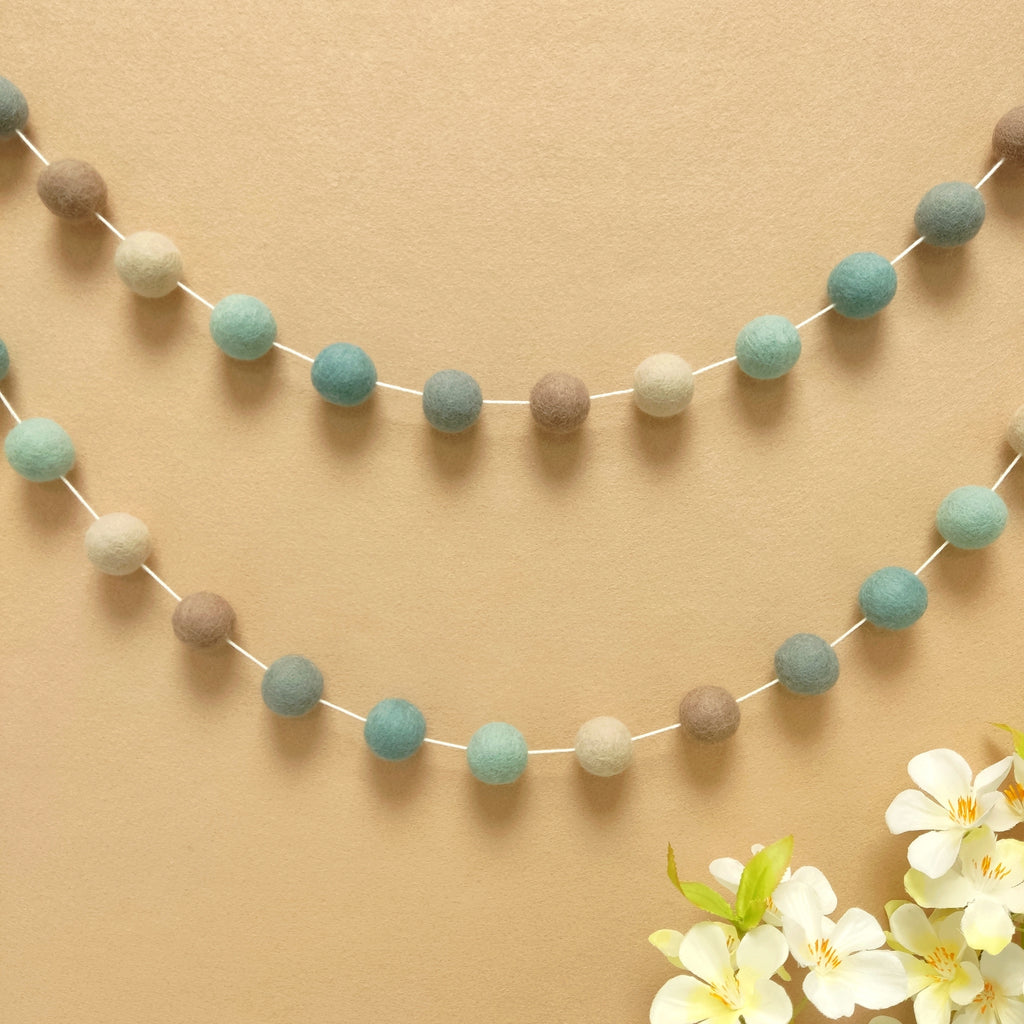 Guirlande pompons bleu beige gris fixée sur un mur
