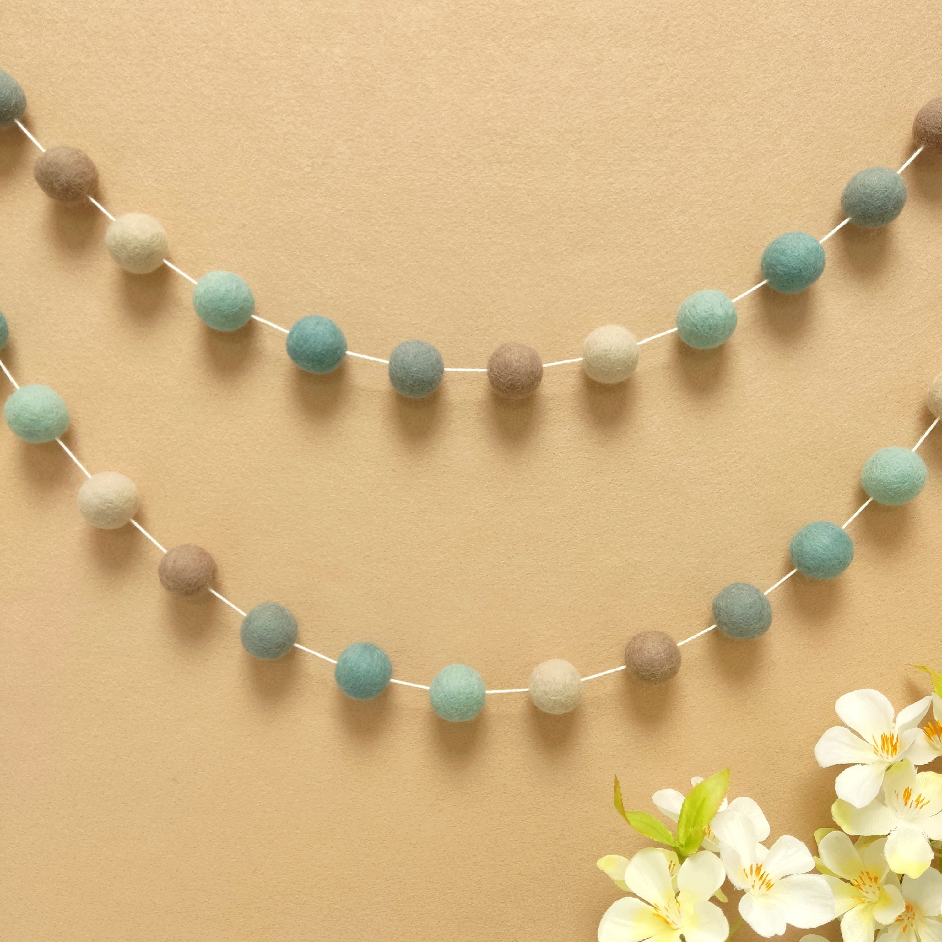 Guirlande pompons bleu beige gris fixée sur un mur