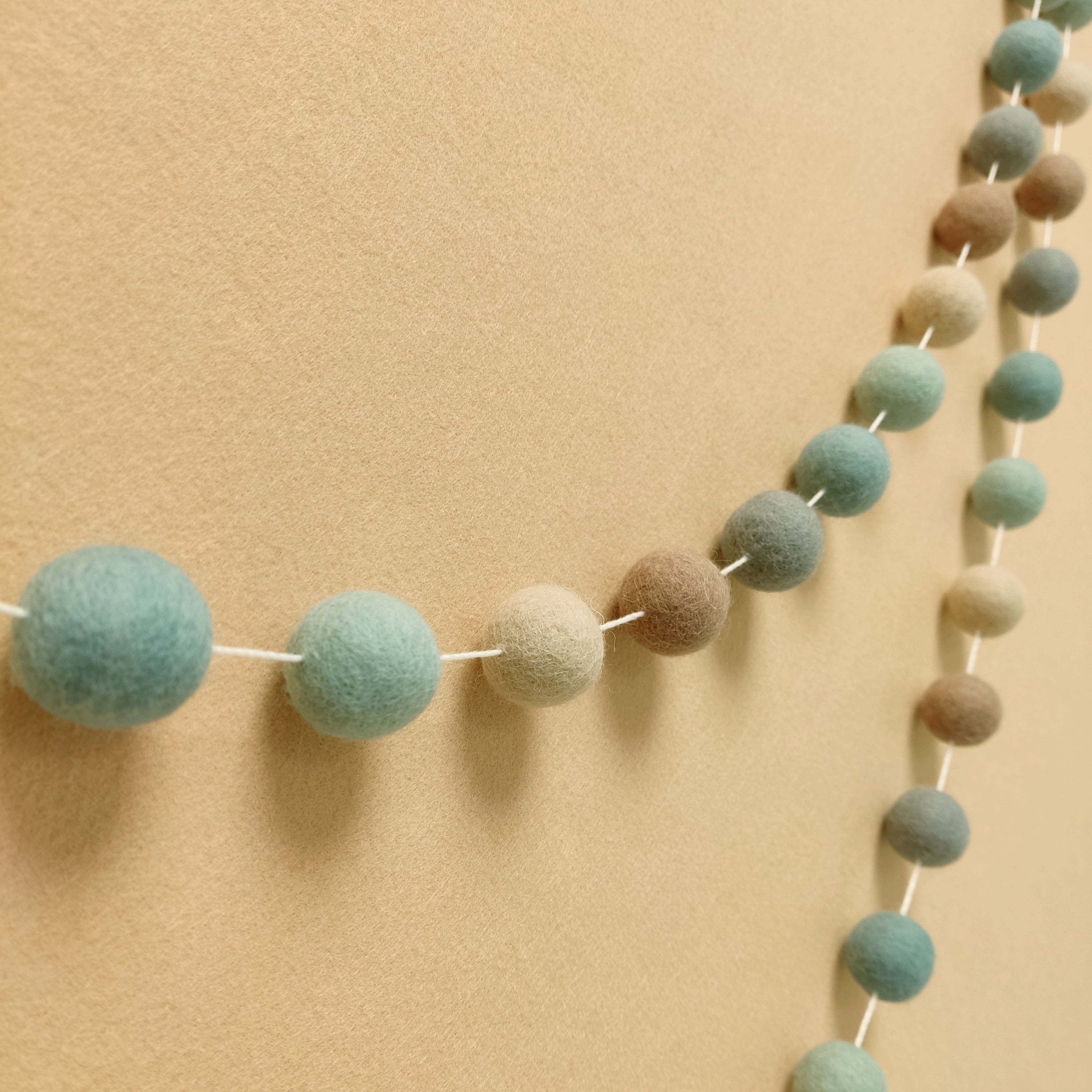 Guirlande en boules de feutre bleu nordique beige cappuccino et gris vue de profil sur un mur