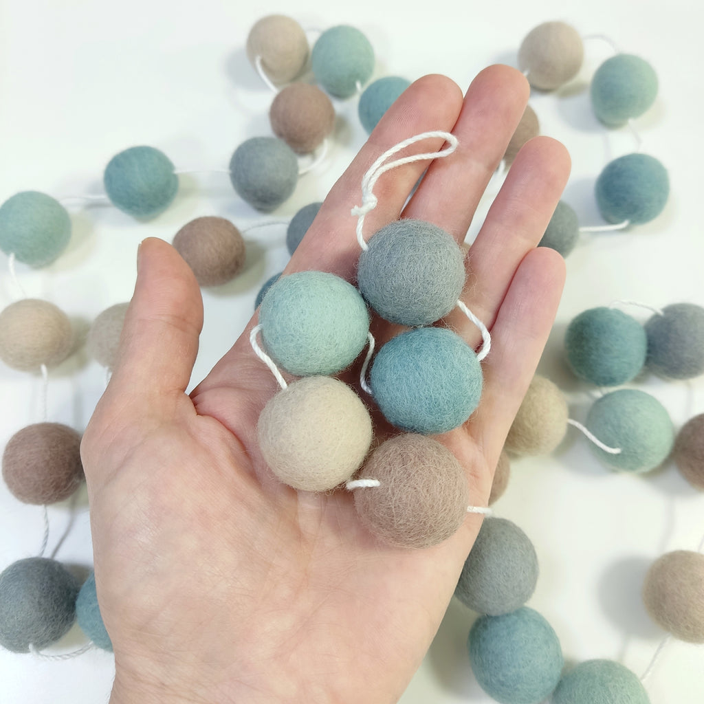 Détail des pompons de feutres de la guirlande bleu beige gris dans une main