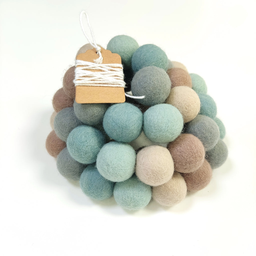 Zoom sur la guirlande de pompons en feutre bleu vert gris beige avec étiquette